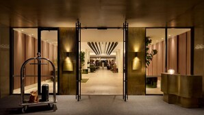 Un vestíbulo de hotel con mostrador de recepción, un carrito de equipaje y un largo pasillo que conduce a las habitaciones.