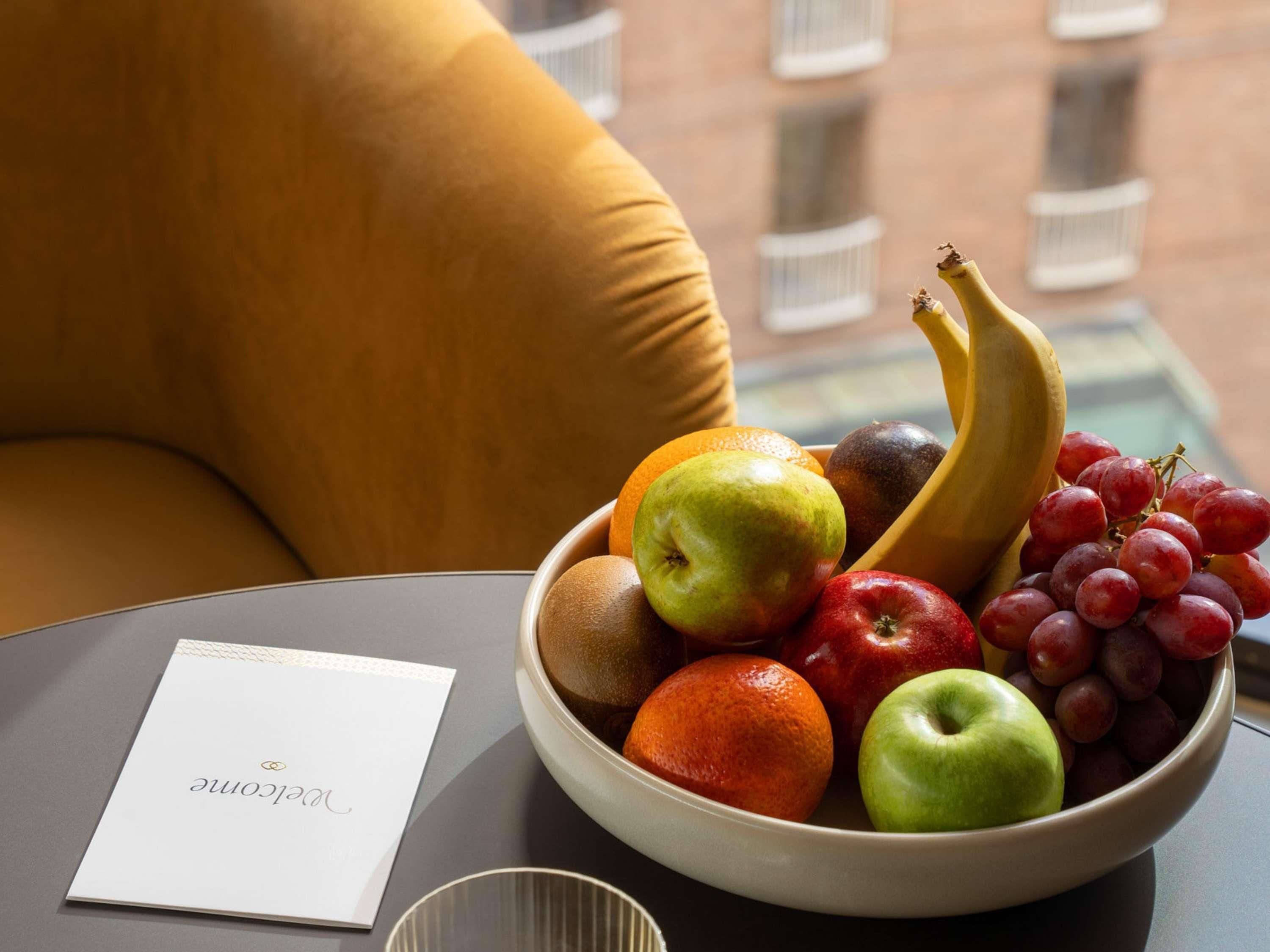 A bowl of fruit on a table with a cushion in the background.