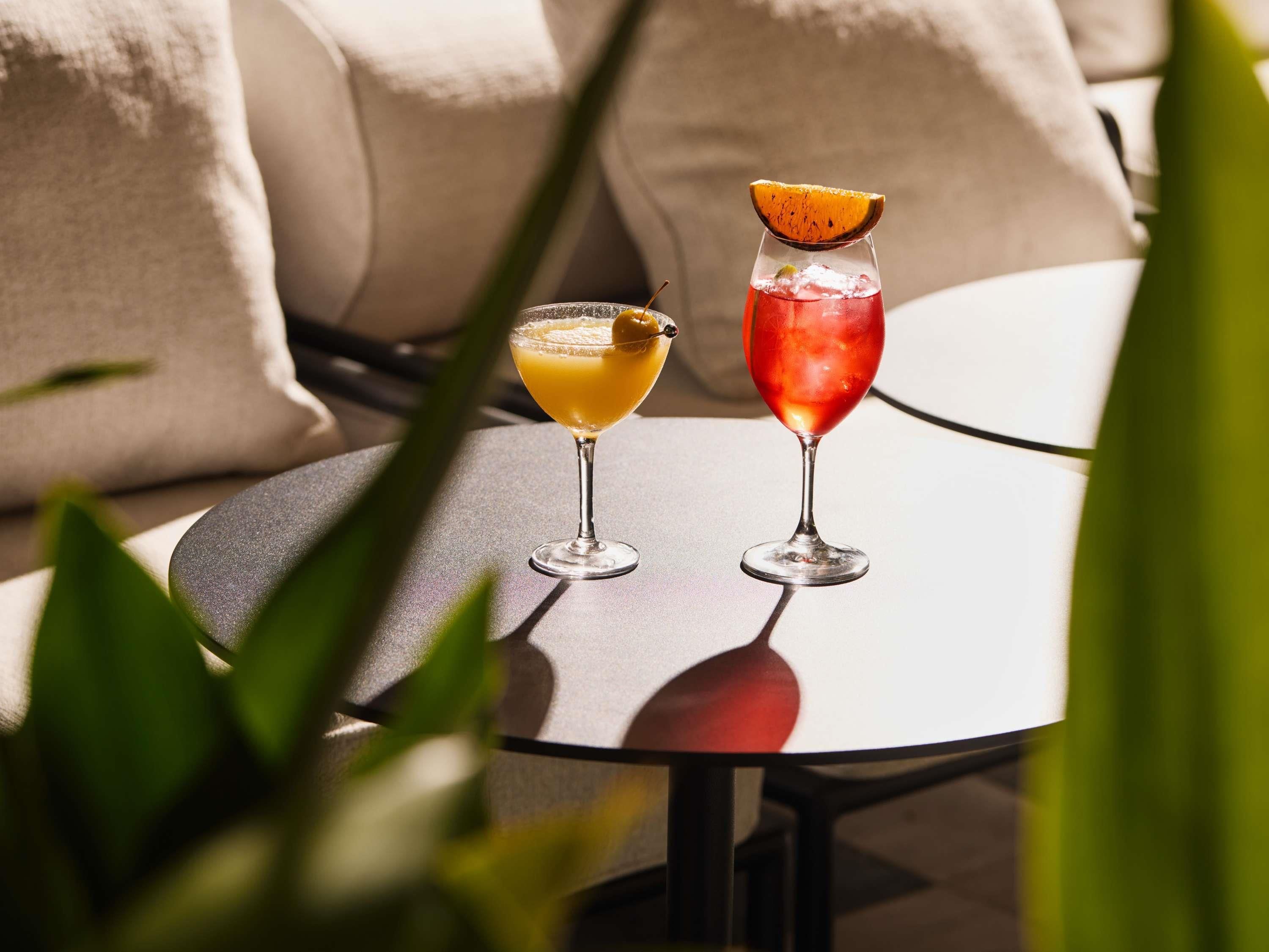 Two cocktails on a round table with a cushion in the background.