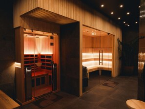 A sauna room with wooden walls and benches, a bench with a towel, and a small trash bin. - Sofitel Sydney Wentworth (Sydney)