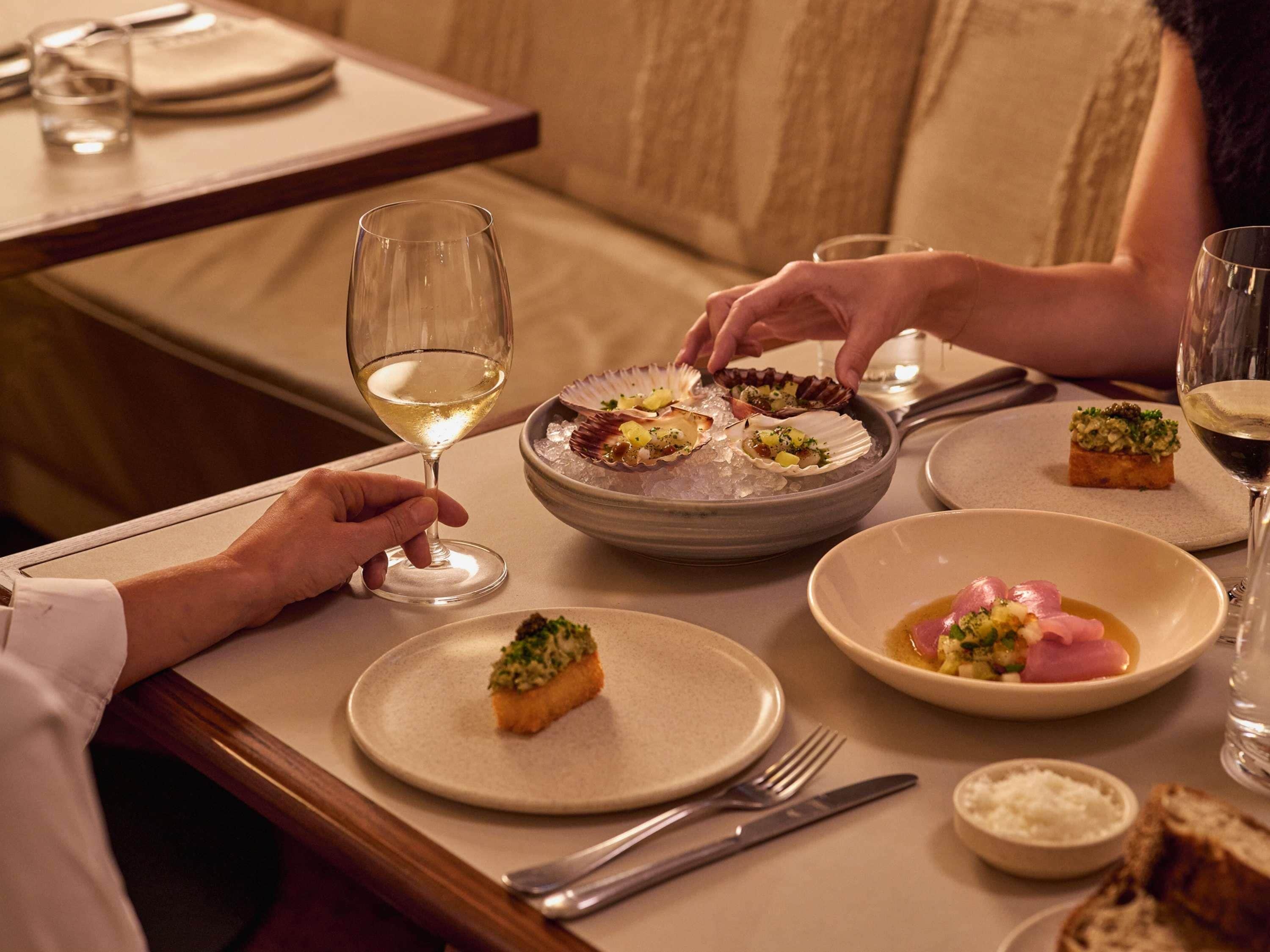 A dining table with plates of food, a glass of white wine, and a bowl of ice.