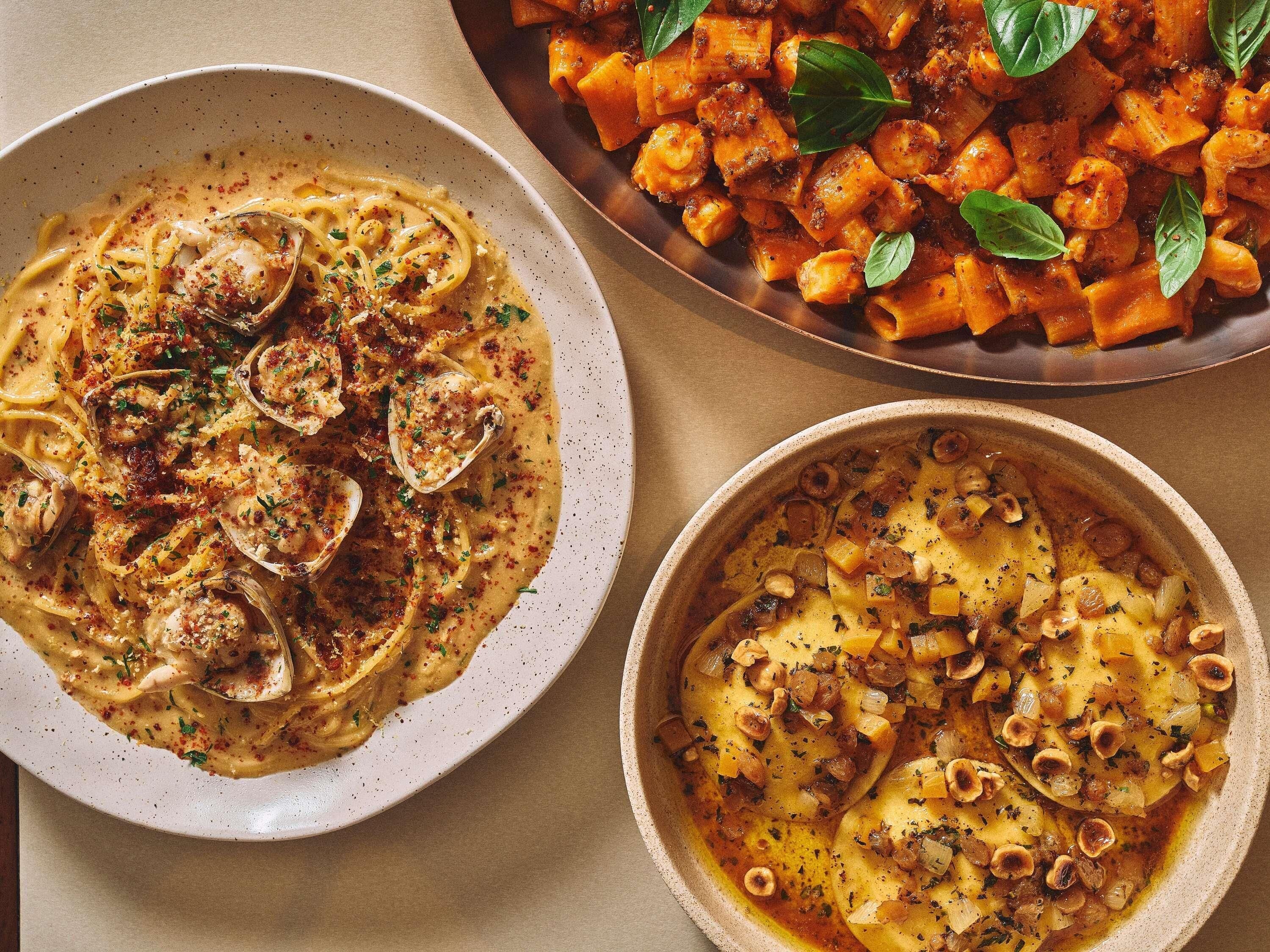 A dining table with three dishes: pasta with clams, a tomato-based dish with pasta, and a creamy potato dish.