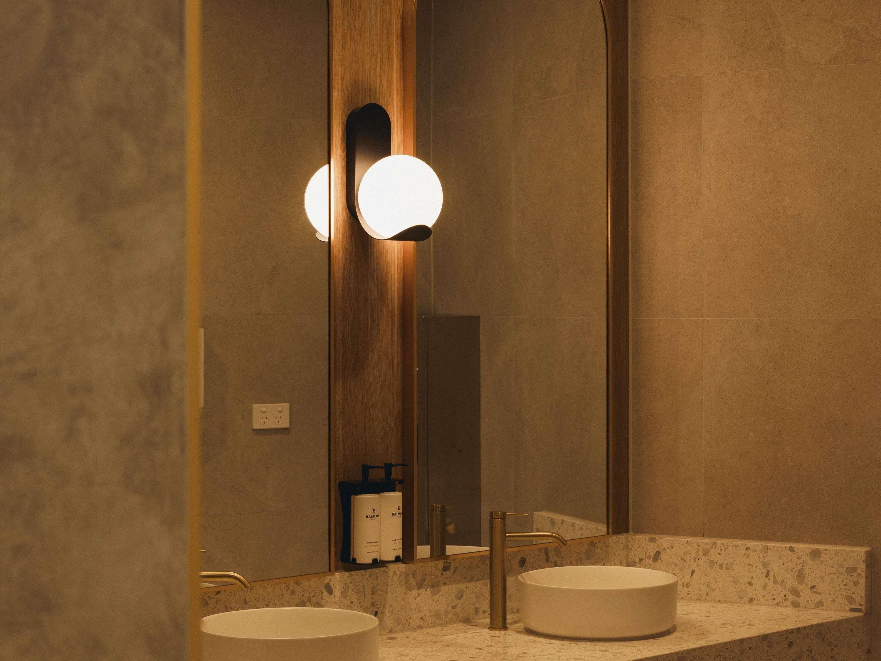 A bathroom with two sinks, a mirror, and wall-mounted lights.