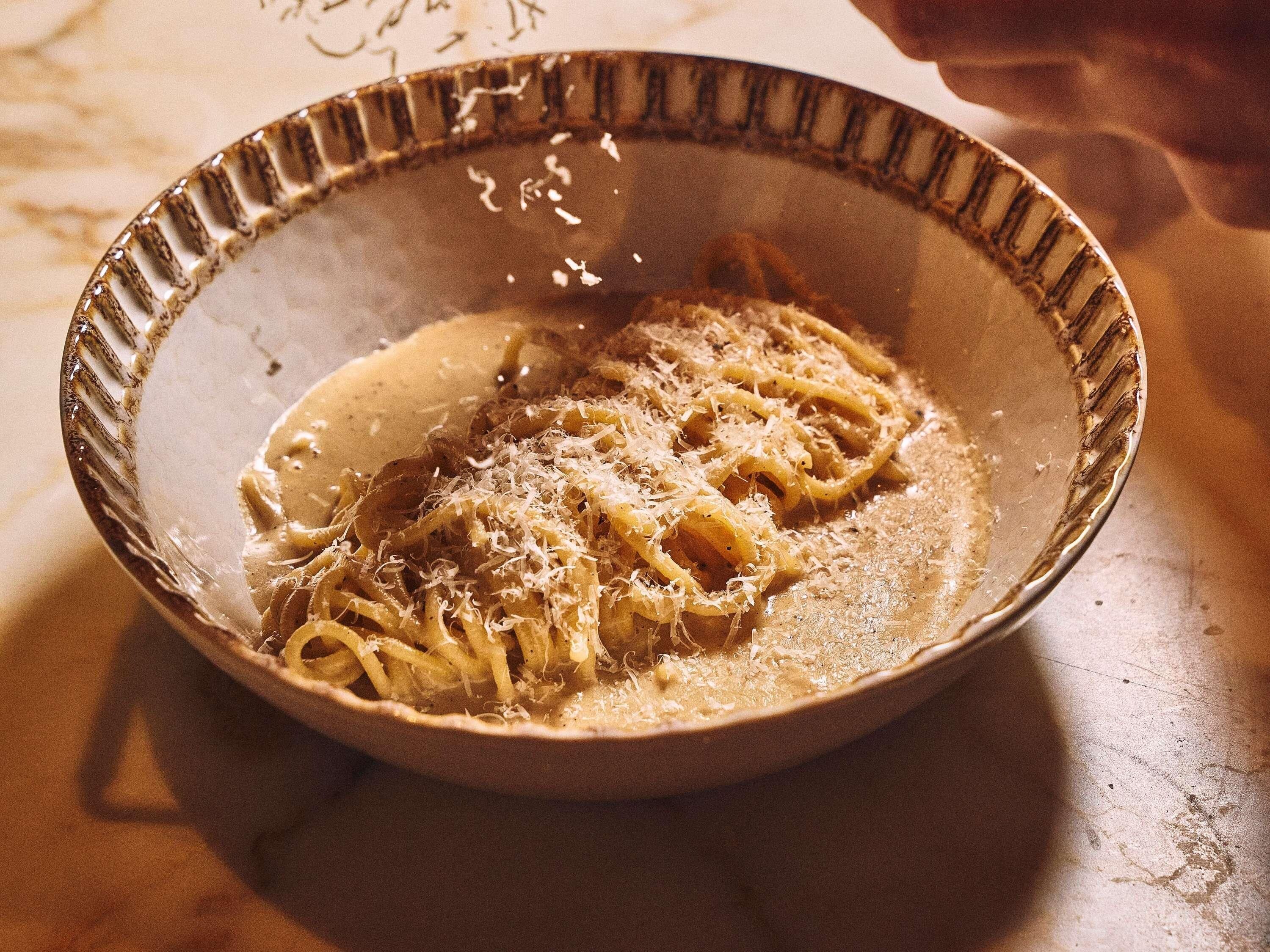 A bowl of pasta with a creamy sauce and grated cheese on a table.