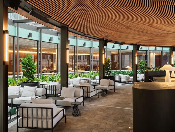 An outdoor seating area with modern furniture, large windows, and indoor lighting. - Sofitel Sydney Wentworth (Sydney)