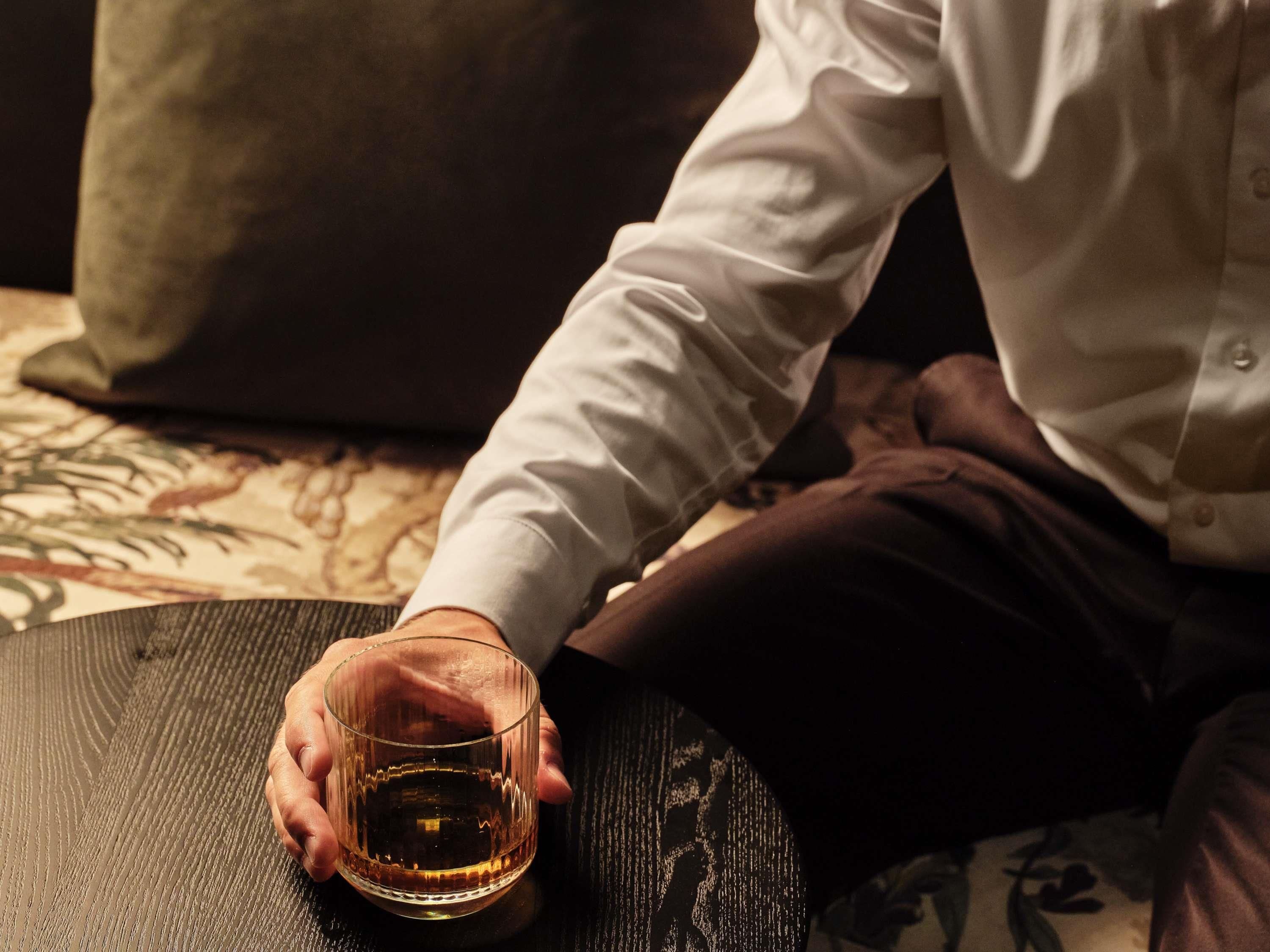 A person holding a glass of whiskey on a round table.
