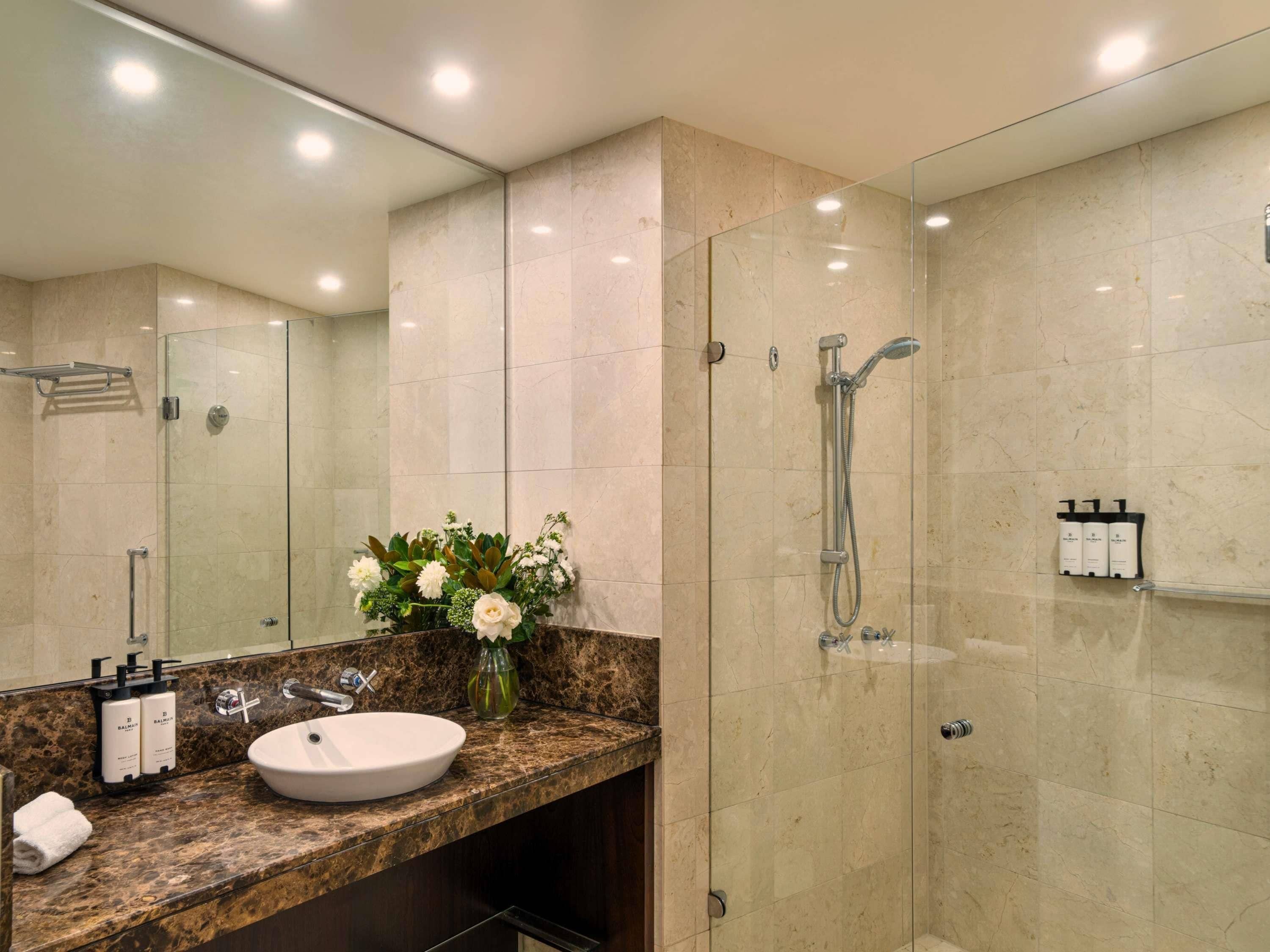 A modern bathroom with a glass-enclosed shower, a marble countertop, and a large mirror.
