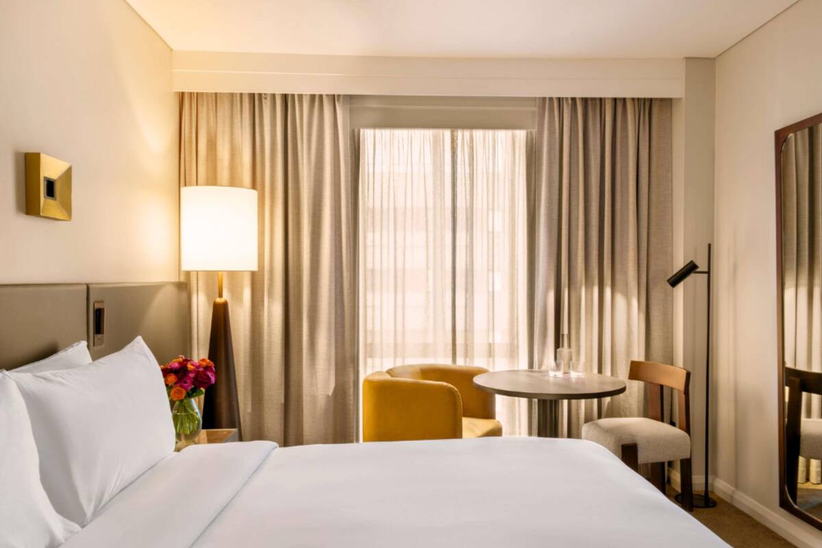 Ein Hotelzimmer mit einem Bett, einem Schreibtisch, einem Sessel und einem Vorhangfenster.