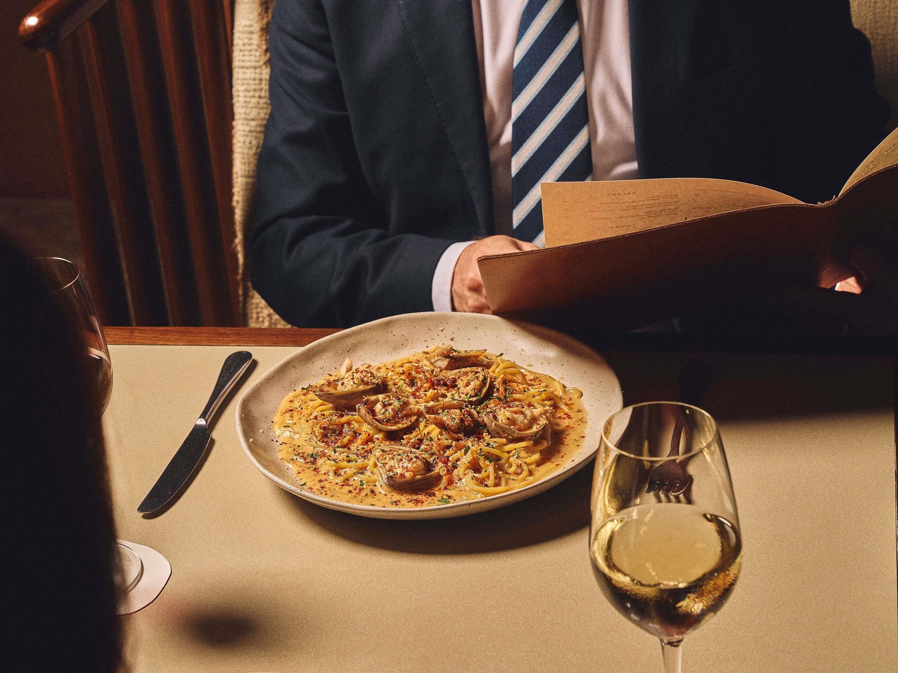 A dining table with a plate of pasta, a wine glass, and a menu.
