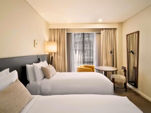 A hotel room with two beds, a small table, a chair, a lamp, and a view of the city through the window. - Sofitel Sydney Wentworth (Sydney)