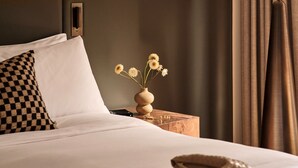 A neatly made bed with white linens, a checkered pillow, a vase with flowers, and a small wooden nightstand with a book and a remote control. - Sofitel Sydney Wentworth (Sydney)