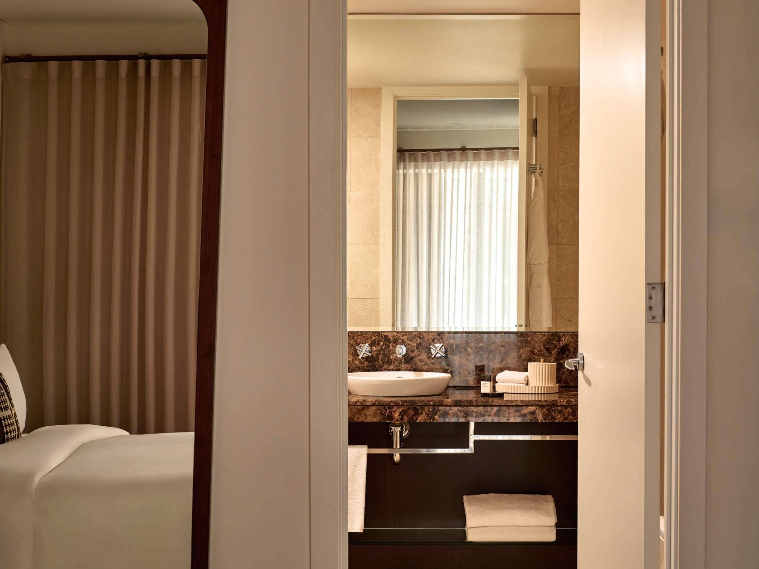 A hotel bathroom with a large mirror, a sink, and a towel rack.