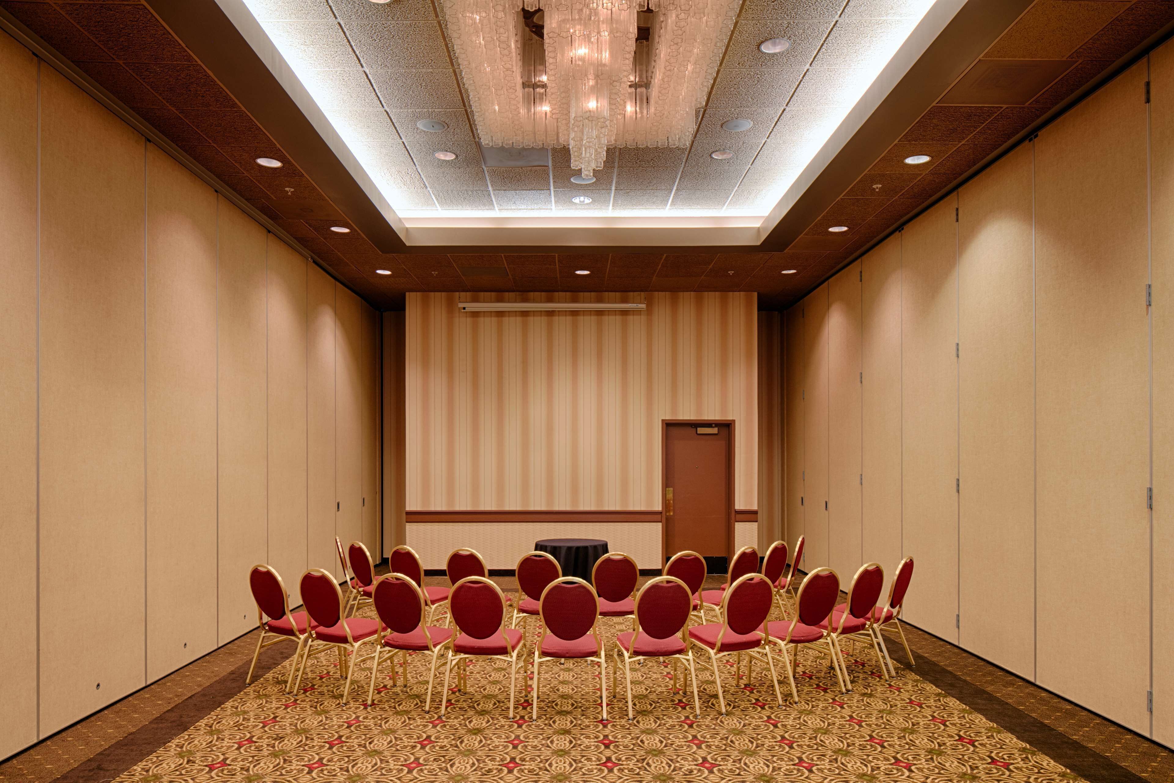 A conference room with a patterned carpet, rows of chairs, a table, and a door.