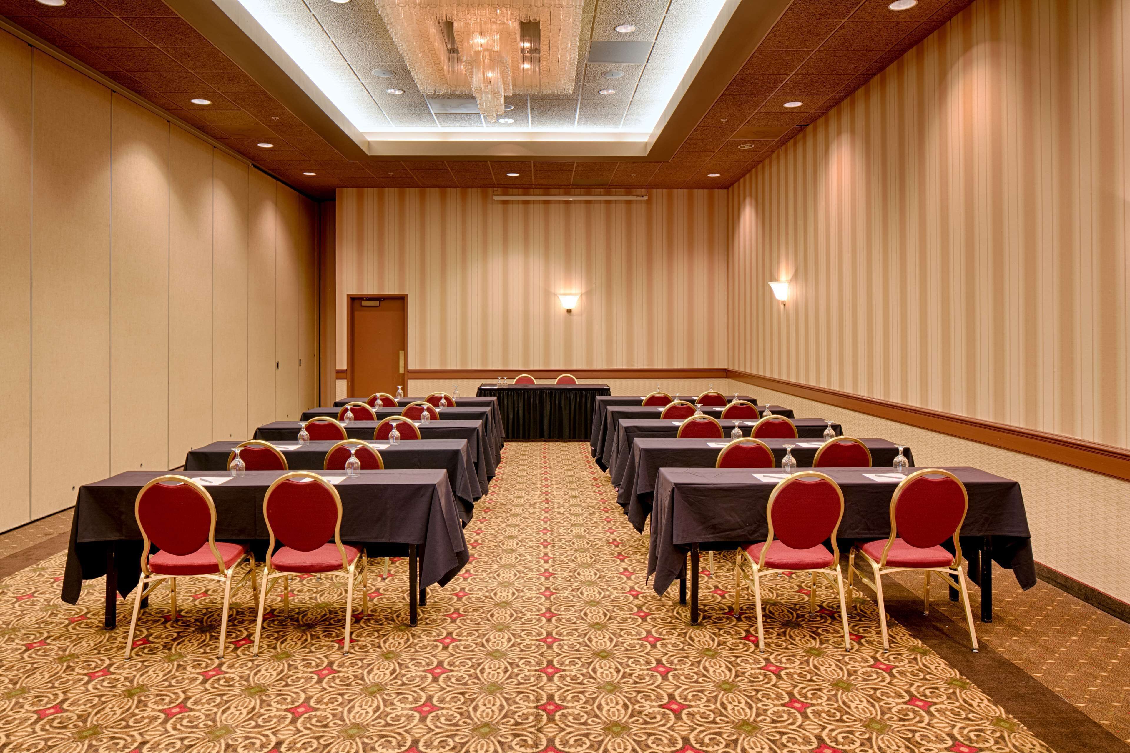 A conference room with rows of tables and chairs, a patterned carpet, and a chandelier.
