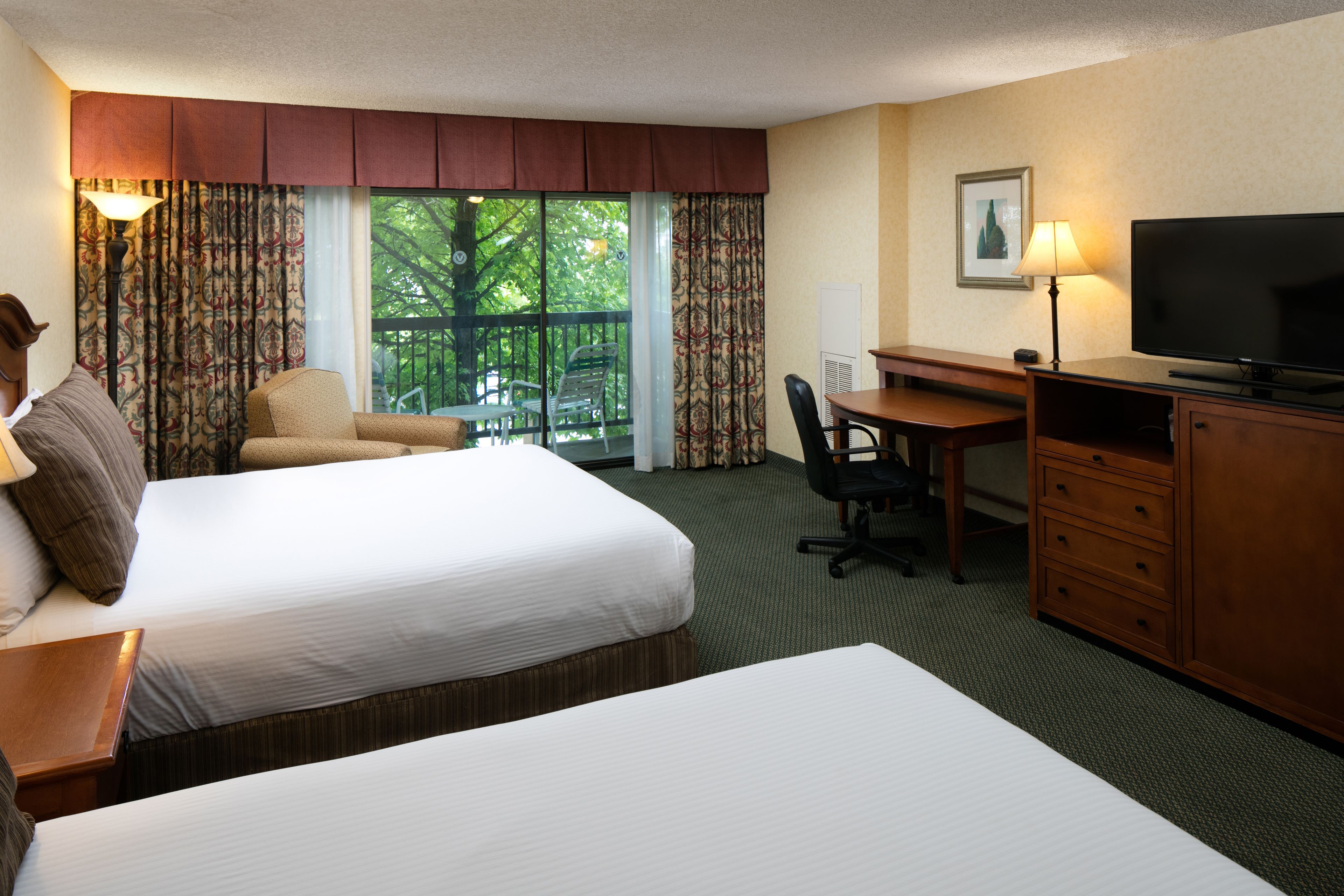 A hotel room with two beds, a desk, a television, and a chair.