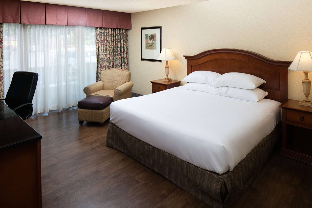 A hotel room with a large bed, a chair, a desk, and a lamp.