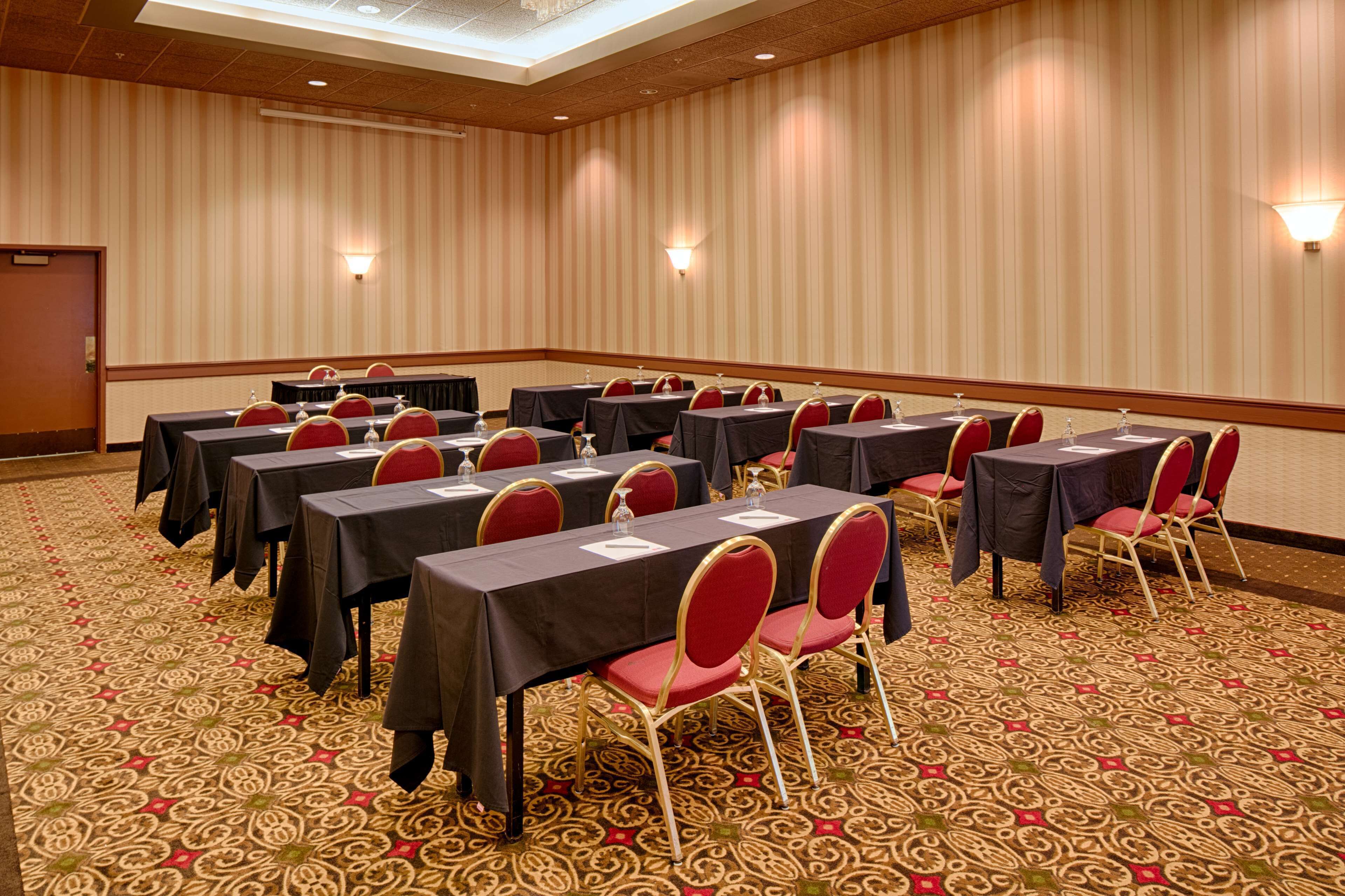 A conference room with multiple tables and chairs, carpeted floor, and wall-mounted lighting.