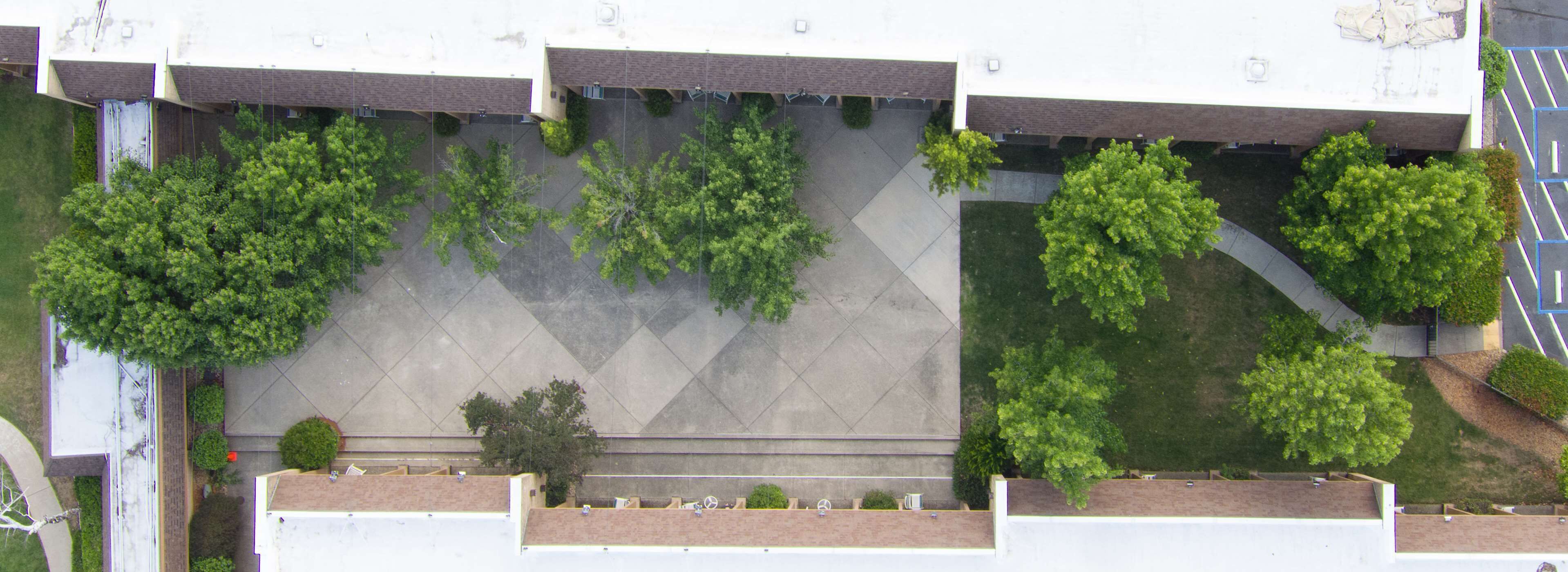 An aerial view of a building with a parking lot, green spaces, and a covered walkway.