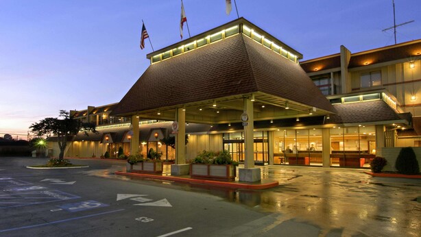 Un hotel con entrada cubierta, varias banderas y un estacionamiento.