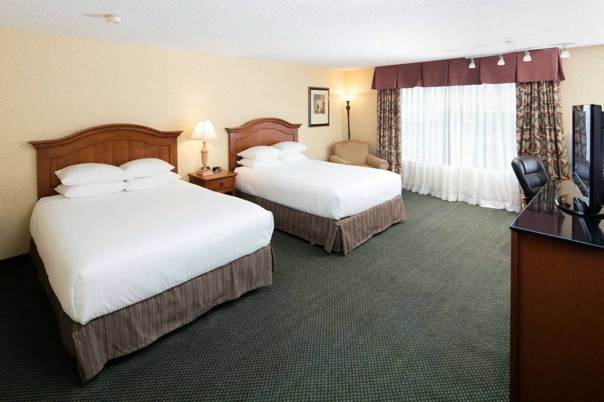A hotel room with two beds, a desk, a chair, and a television.