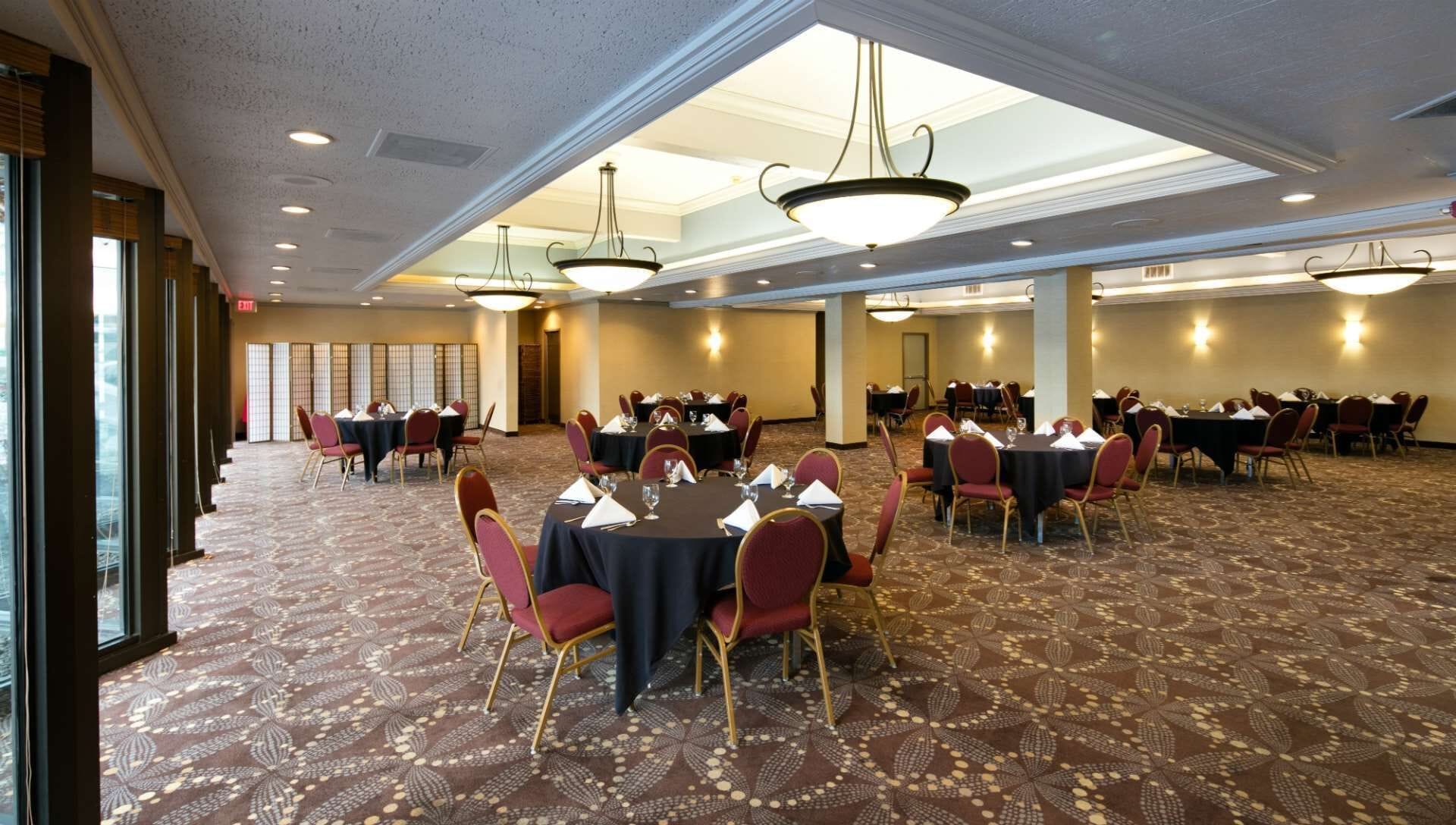 A large conference room with multiple tables and chairs, arranged in rows.