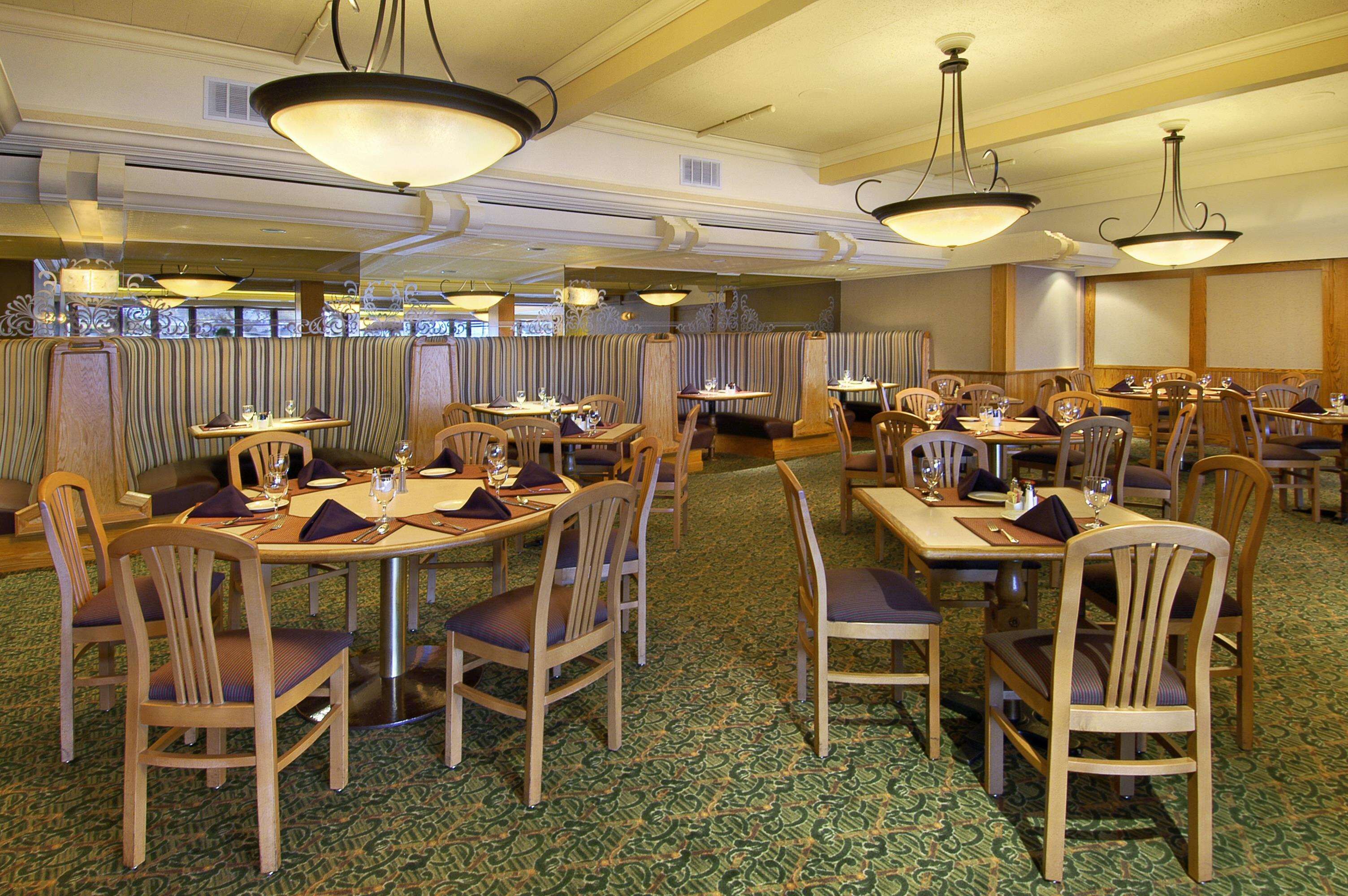 A dining area with multiple tables and booths, wooden chairs, and patterned carpet.