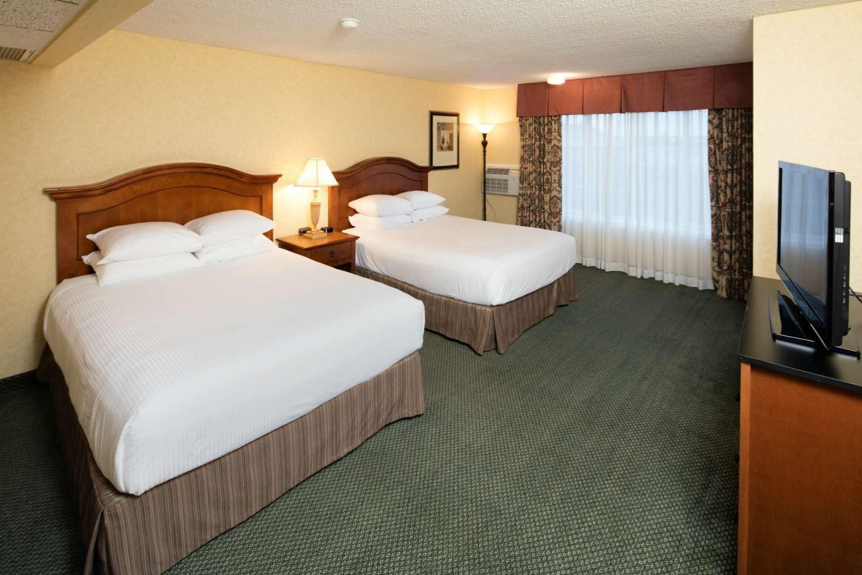 A hotel room with two beds, a television, a lamp, and a framed picture on the wall.