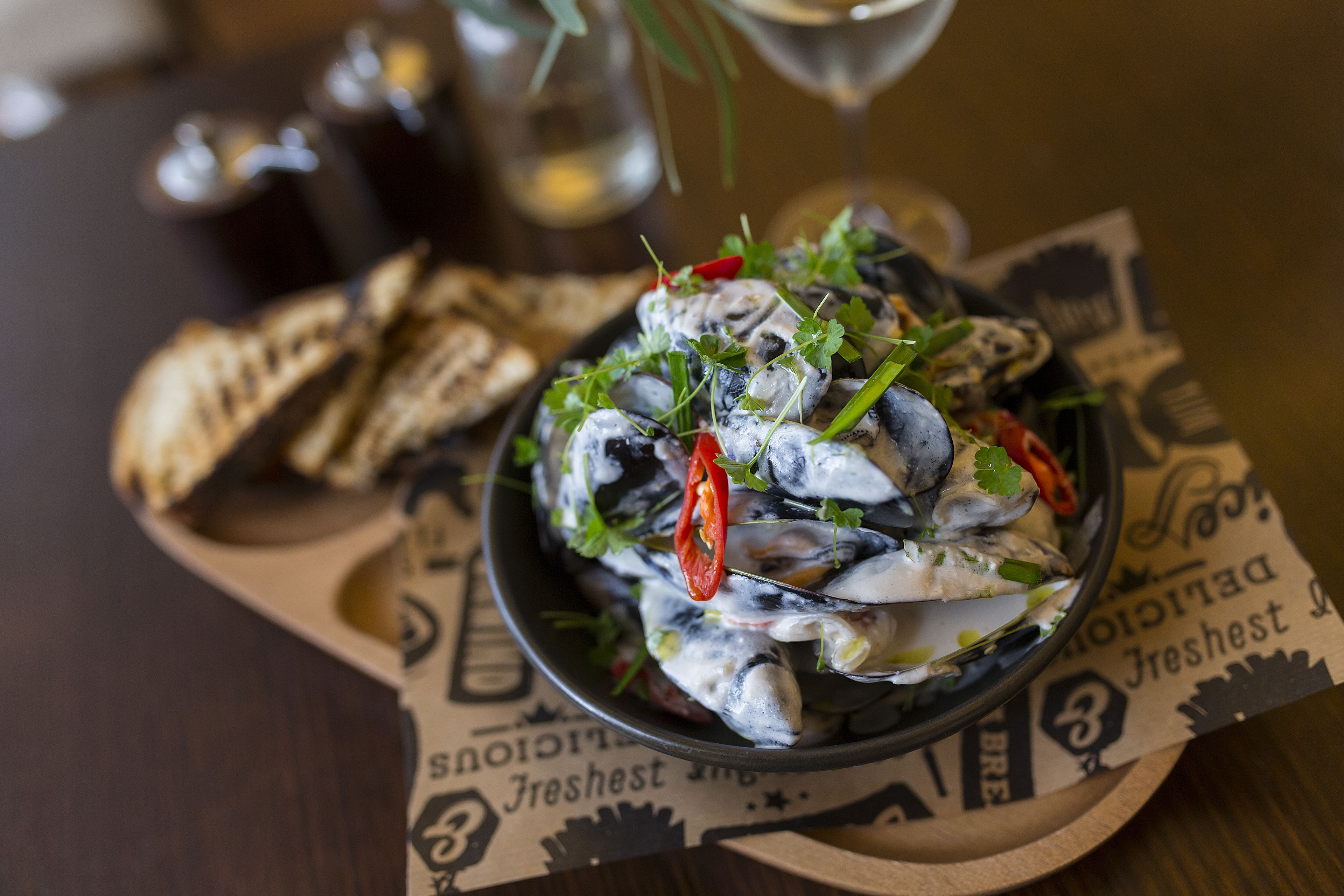 A bowl of seafood salad with herbs and red chili peppers, served on a plate with a newspaper underneath.