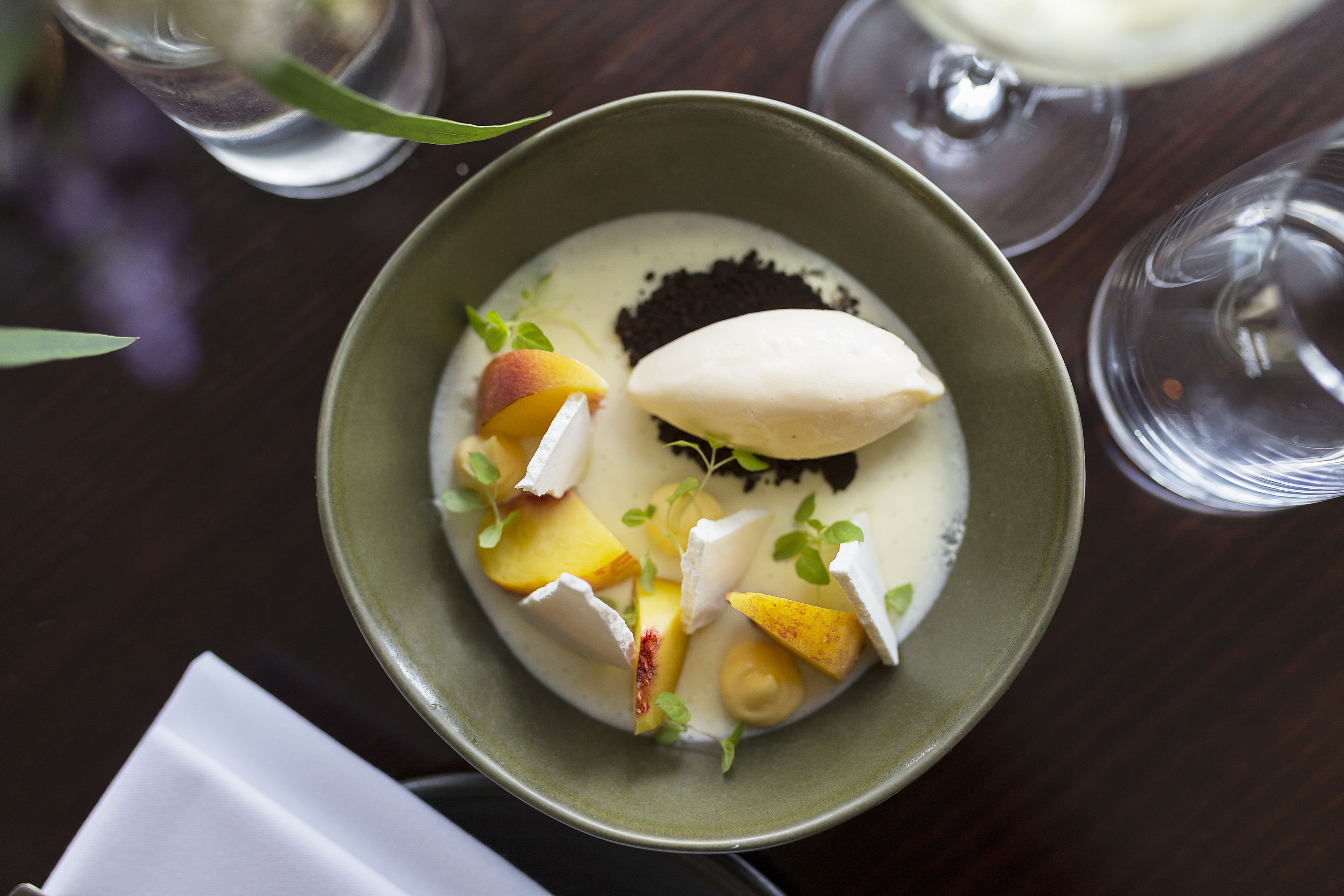 A dessert in a bowl with fruit pieces and a dollop of cream.