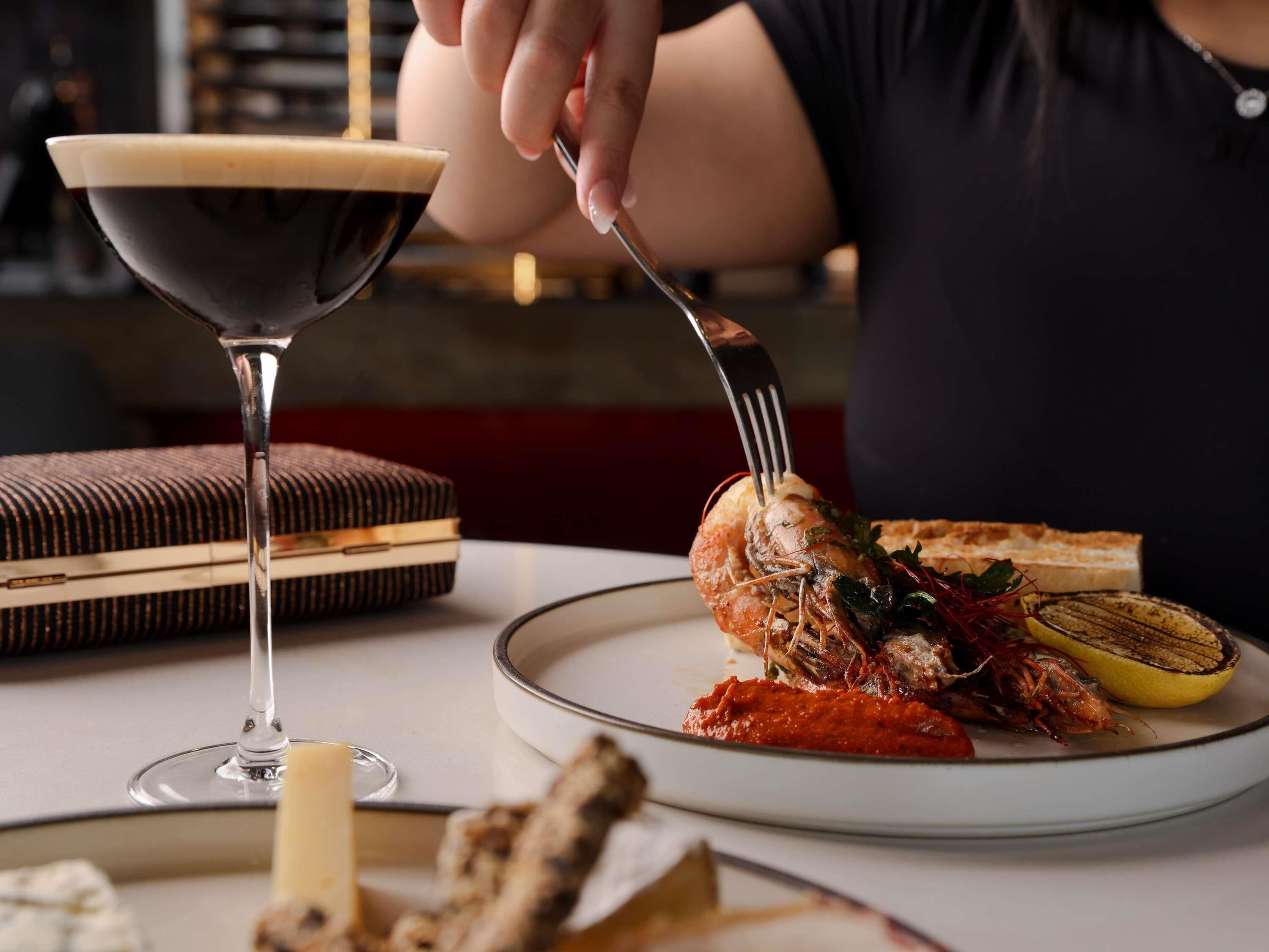 A dining table with a plate of food, a glass of drink, and a fork.