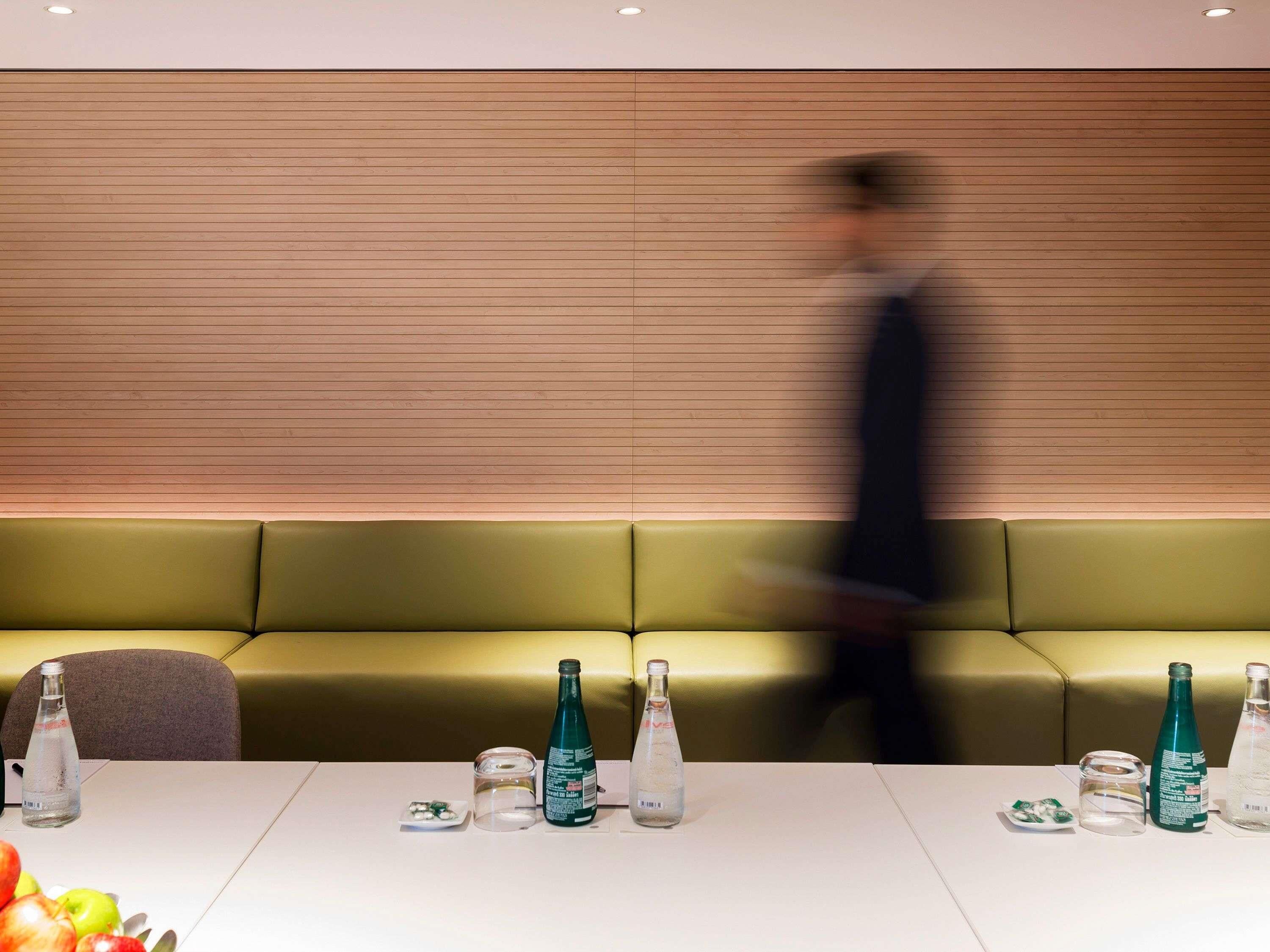 Habitación de hotel con sofá verde, una mesa con botellas y un vaso, y una figura borrosa al fondo.