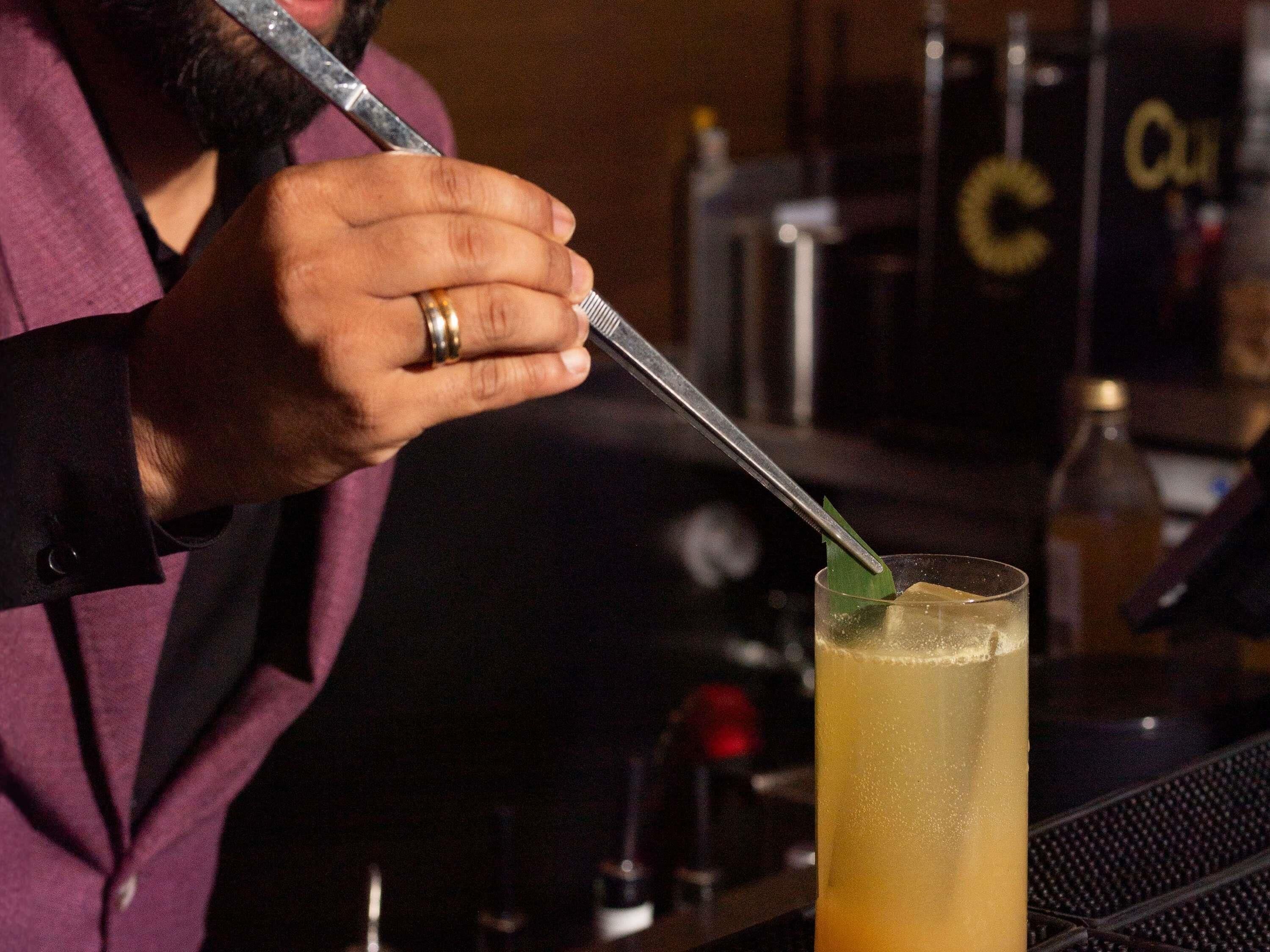 A person stirring a drink in a glass with a spoon.