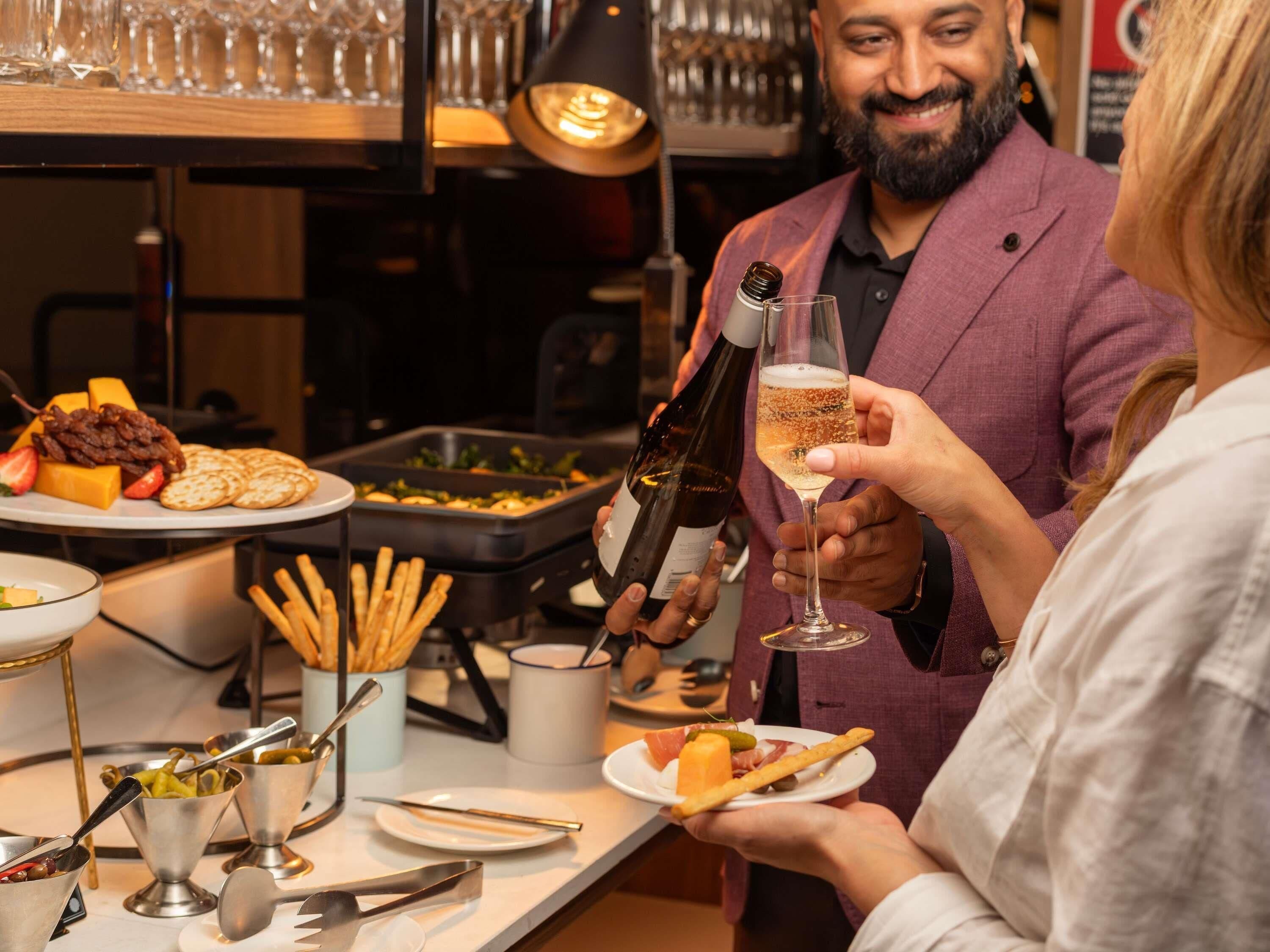 A bar area with a variety of food items and a person holding a bottle of wine.