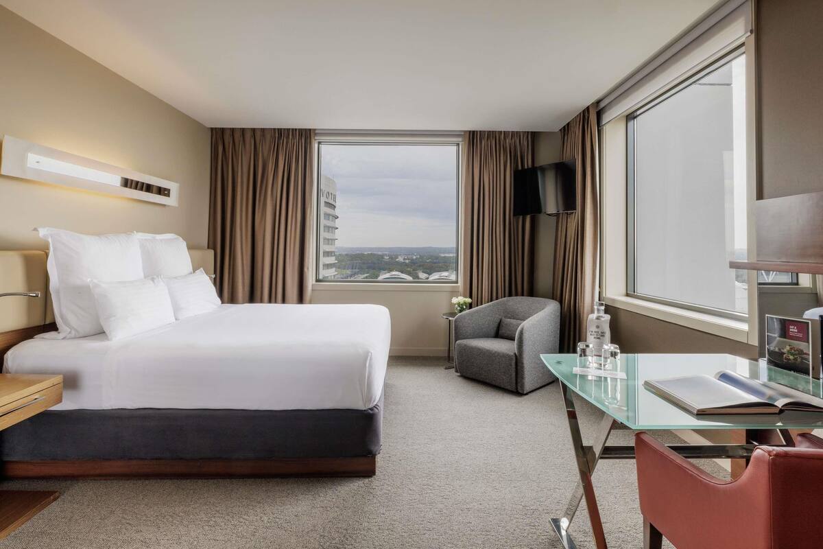 Habitación de hotel con cama, escritorio, silla, televisor y ventana con cortinas.