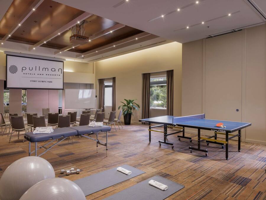 A conference room with a pullman branded screen, exercise balls, a massage table, and a ping pong table.