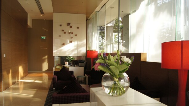 A modern lobby with a reception desk, seating area, and a large window with natural light.