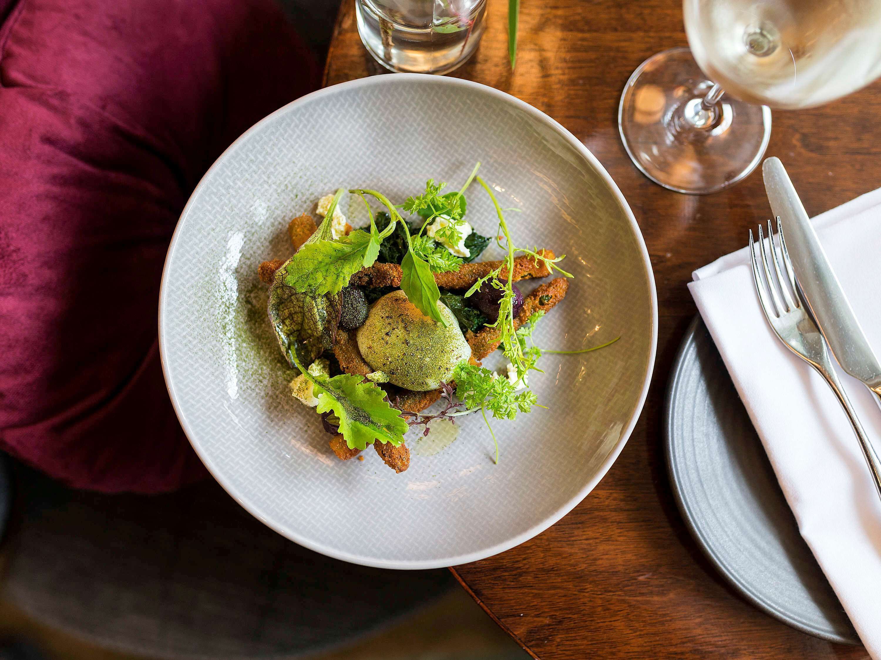 A plate of food on a table with a glass of white wine and a fork.