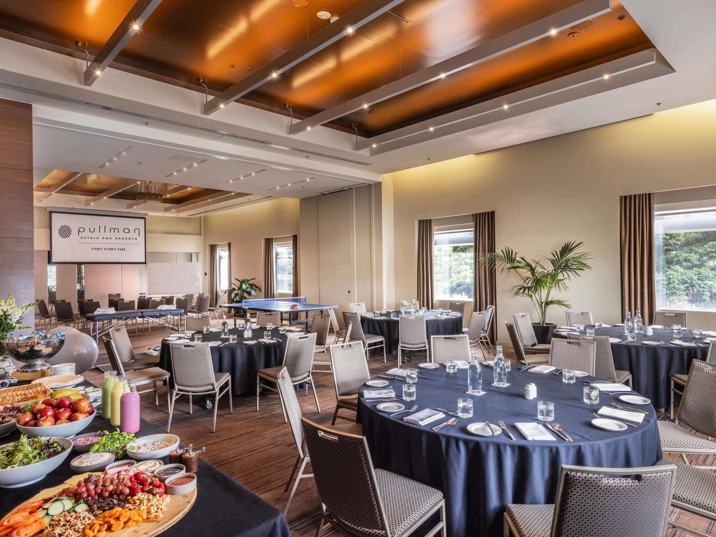 A hotel conference room with tables set for dining, a pullman sign, and a large screen.