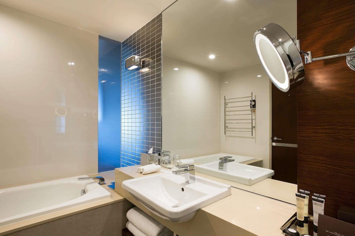 A modern bathroom with two sinks, a bathtub, and a mirror with integrated lighting.