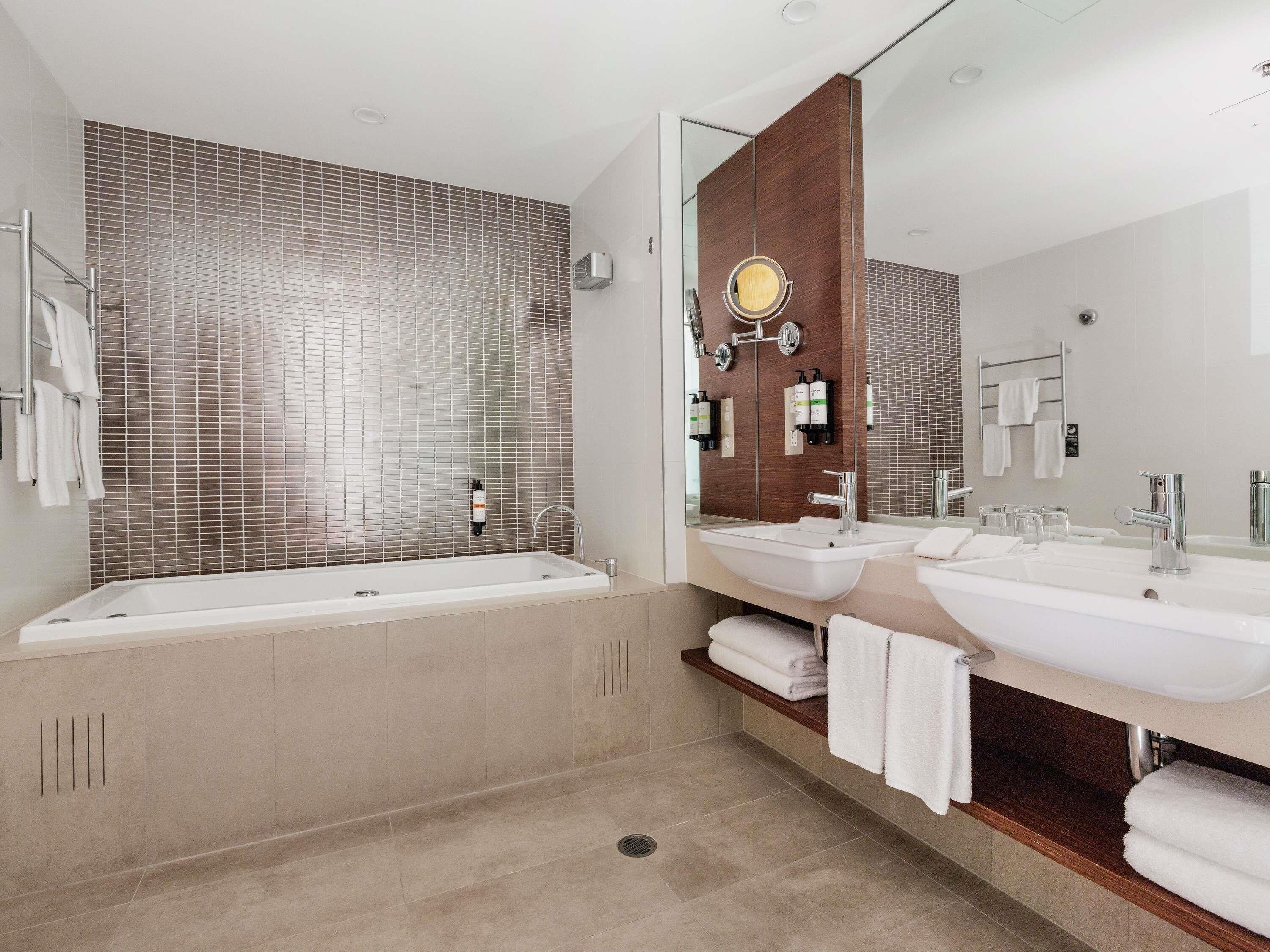 A modern bathroom with a large bathtub, two sinks, and a mirror.