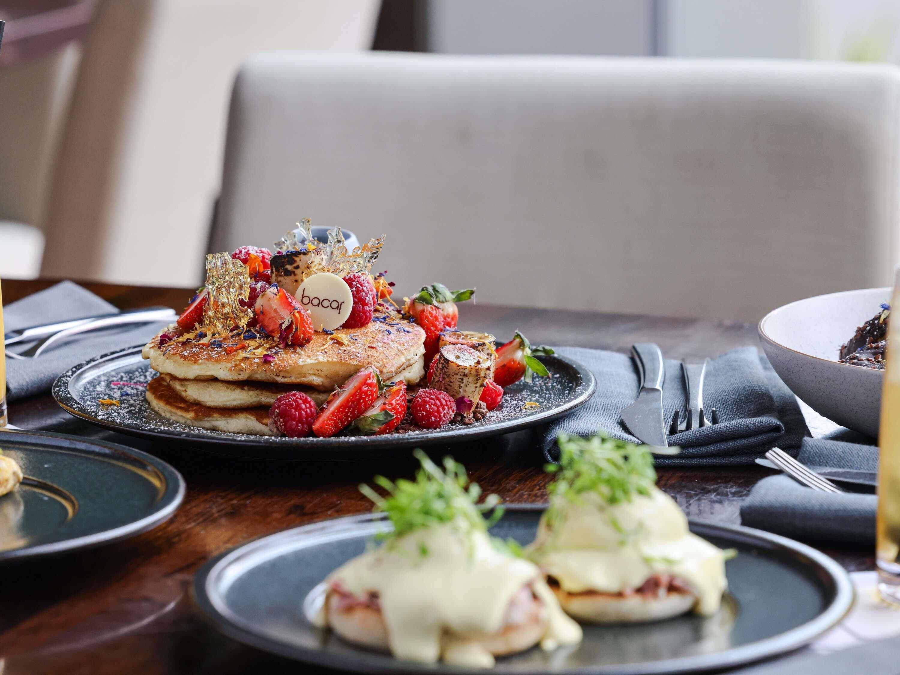 A breakfast setting with pancakes, strawberries, raspberries, and a dessert plate.