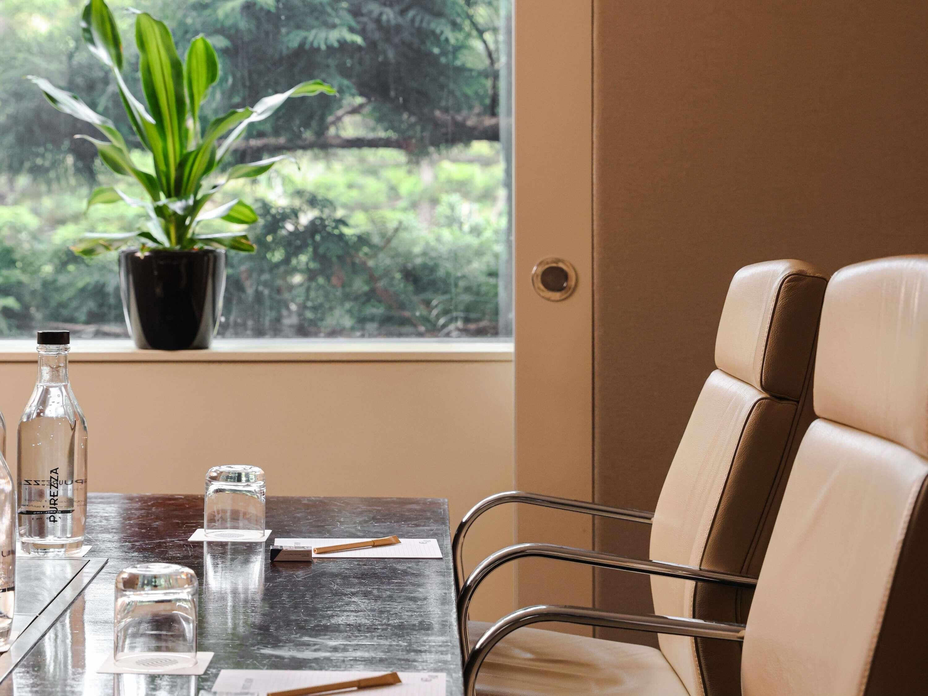 A hotel room with a window view, a table with a bottle, salt, and a pen, and a chair with leather upholstery.