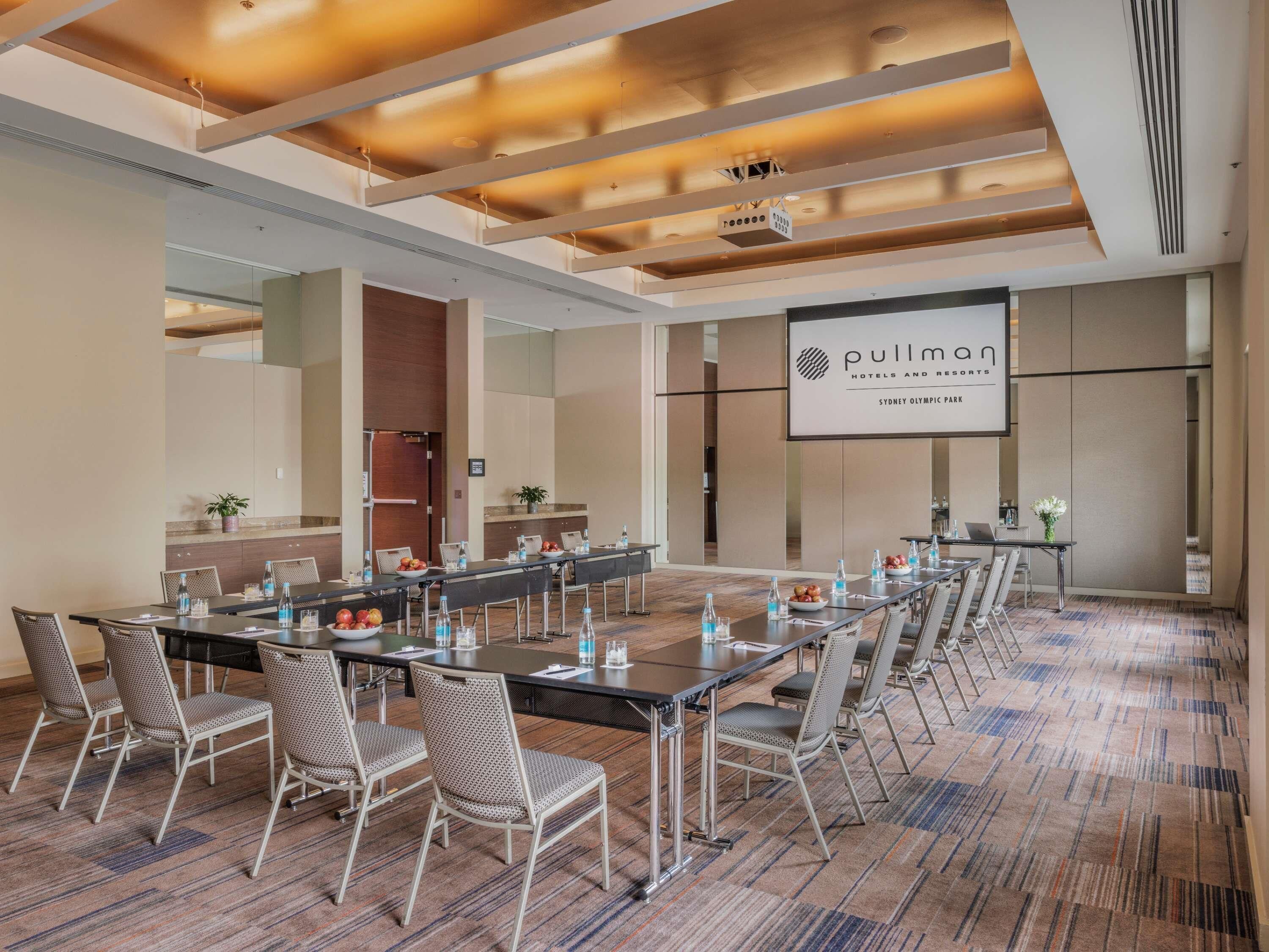 A conference room with a long table, chairs, and a screen displaying 'Pullman Hotels and Resorts Sydney Olympic Park' branding.