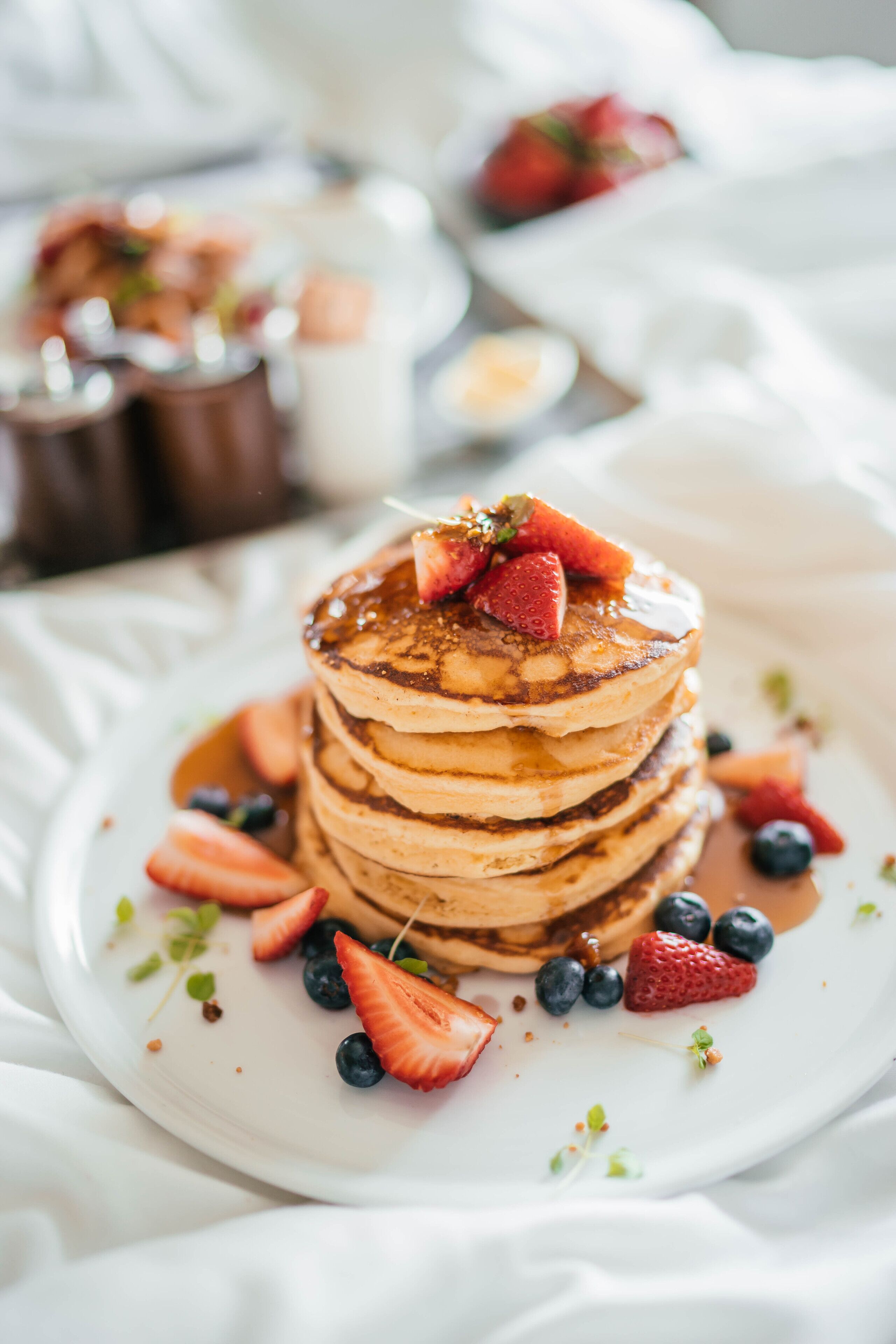 A stack of pancakes with strawberries and blueberries on a white plate.