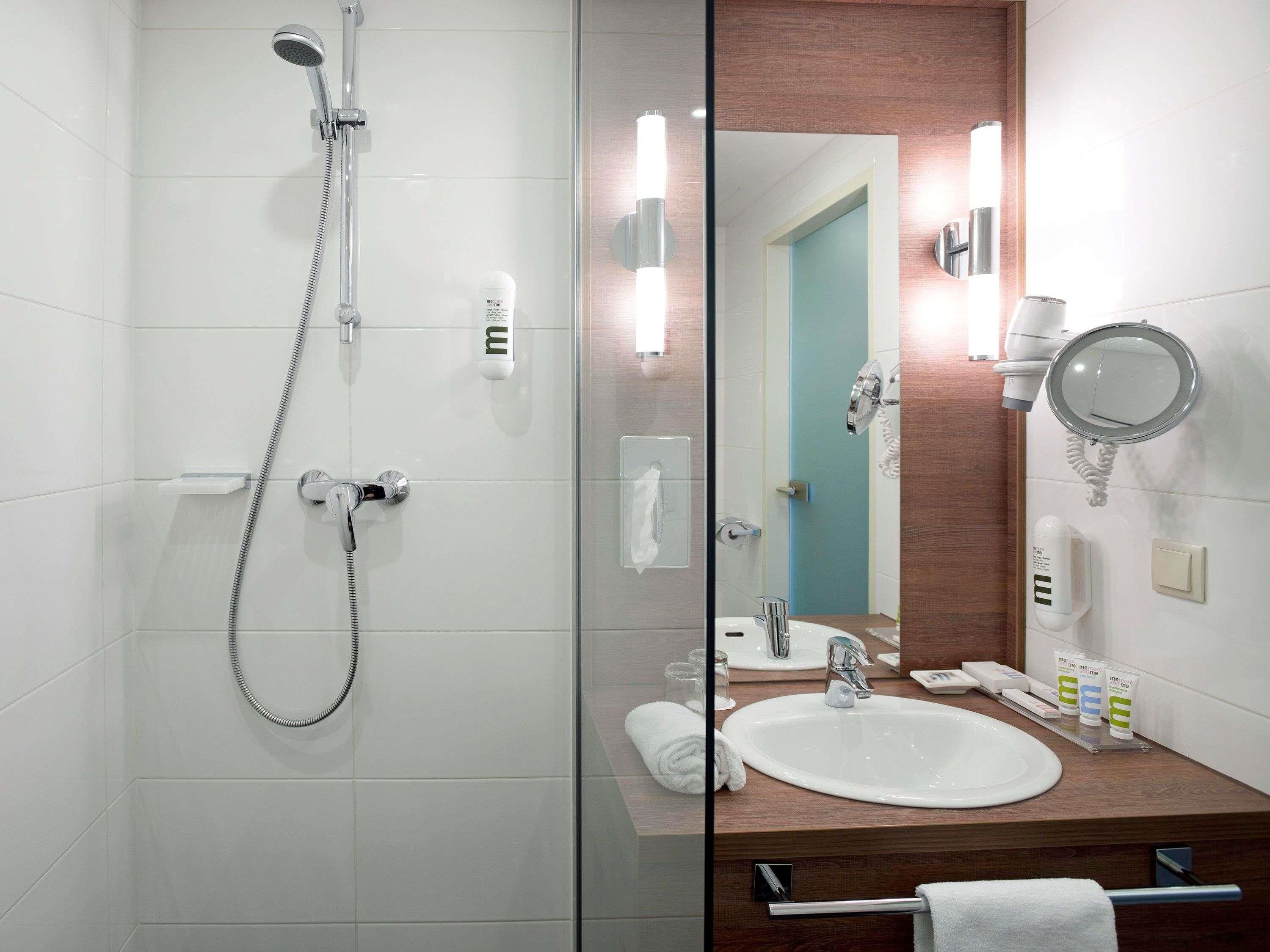 A modern bathroom with a glass shower enclosure, a sink with a mirror, and toiletries.