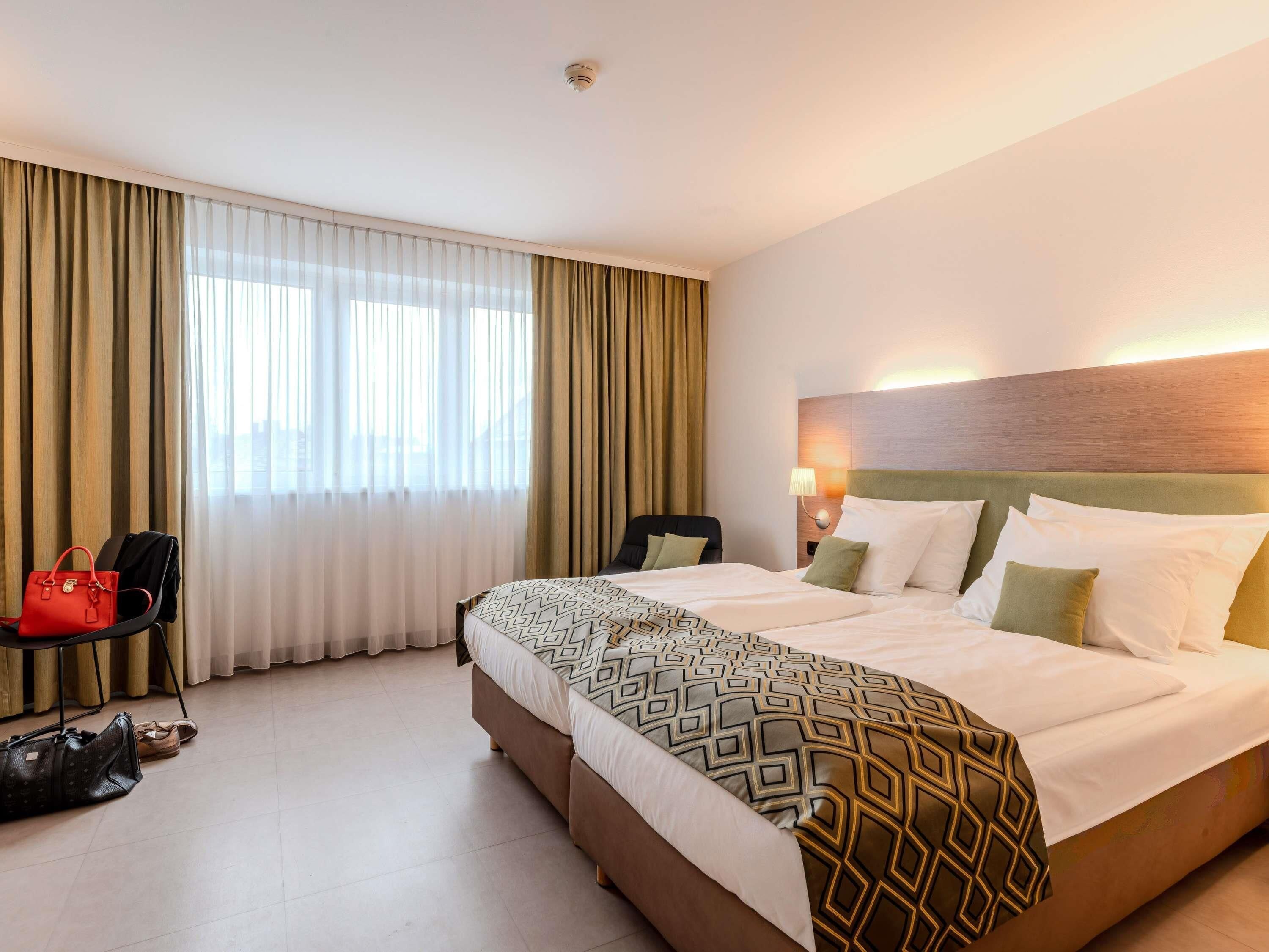 A hotel room with a large bed, a desk, a chair, and a handbag.