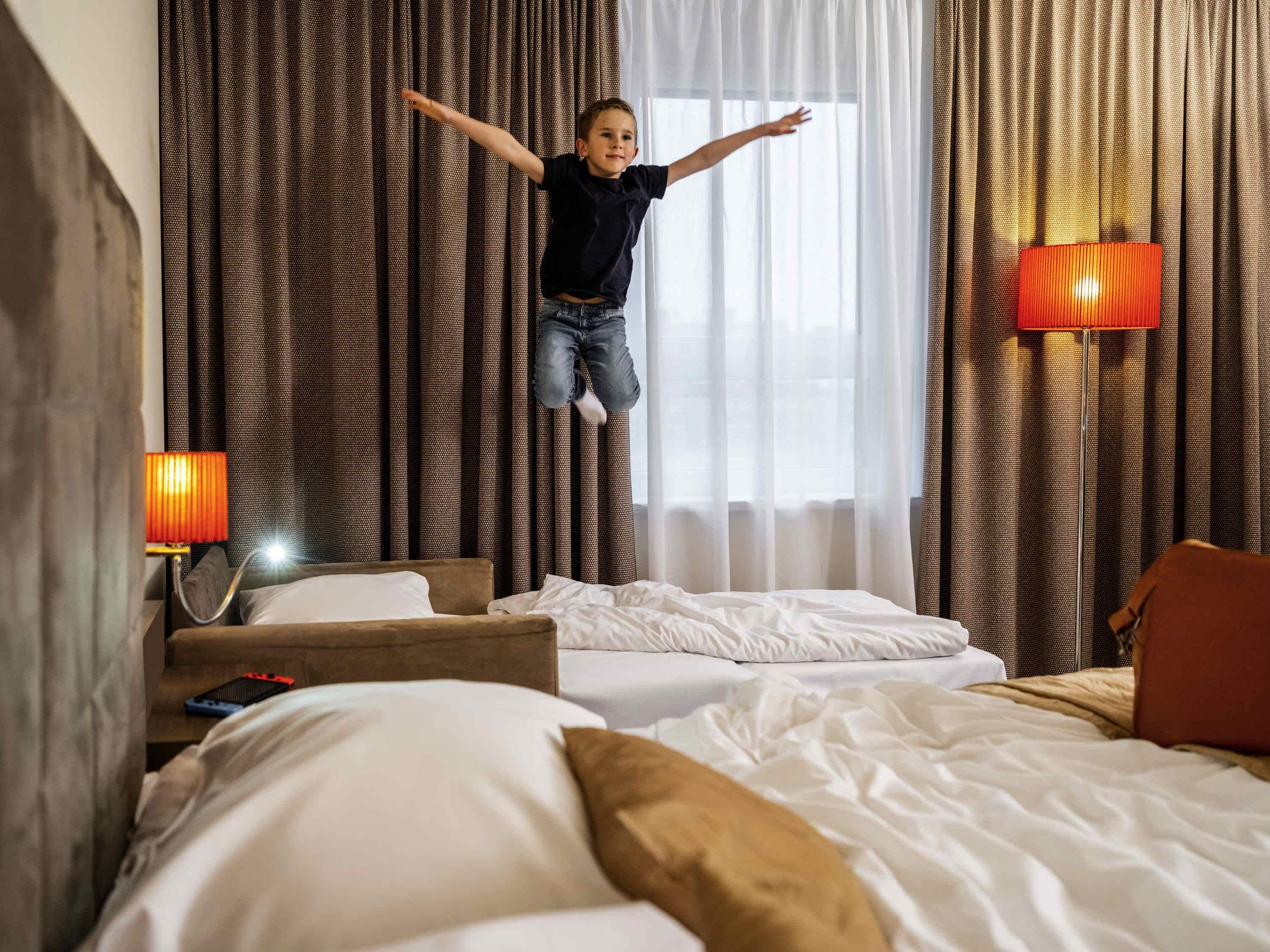 A hotel room with a bed, a nightstand, a lamp, and a window with curtains.