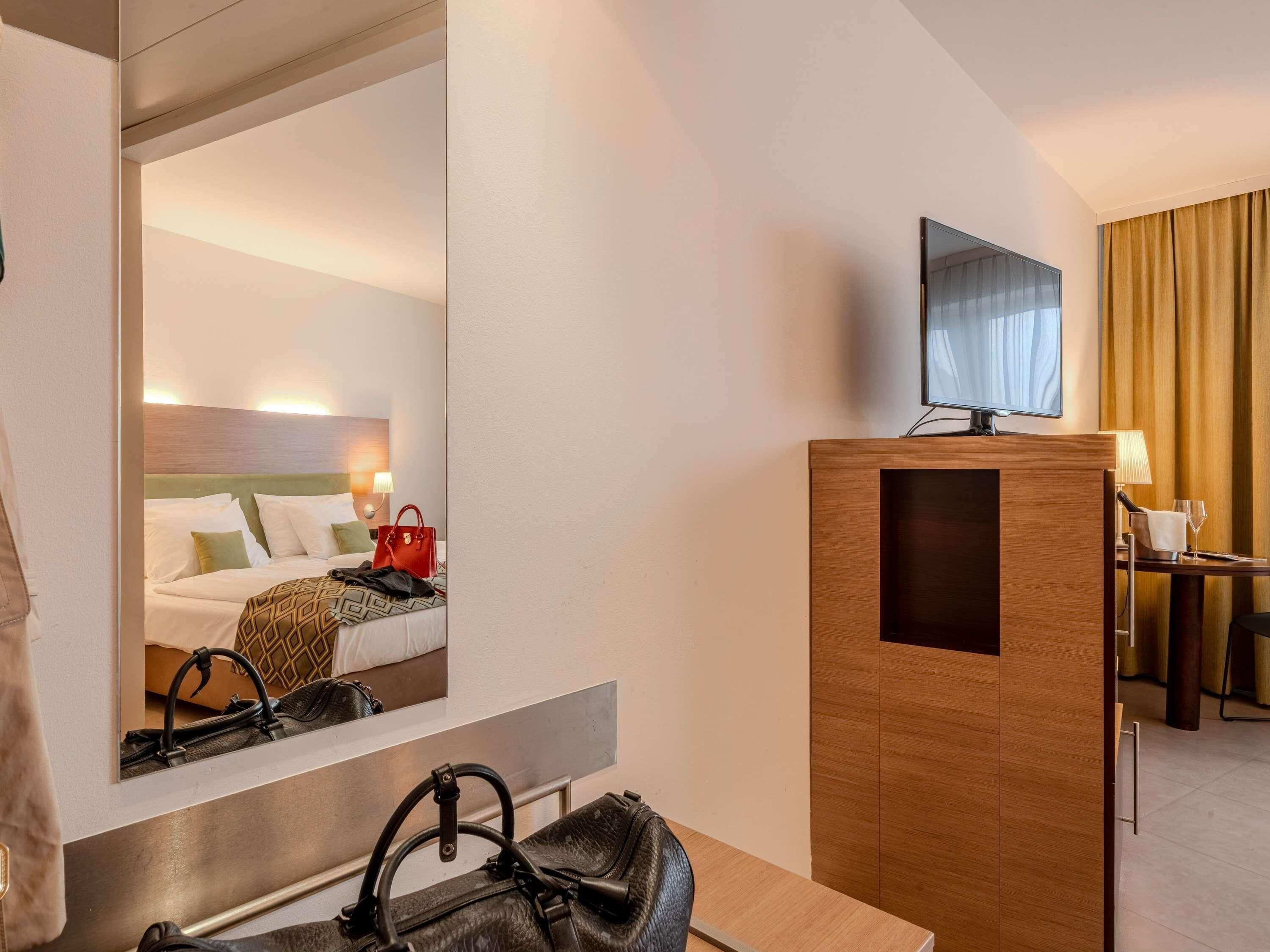 A hotel room with a large mirror reflecting the bed and a television on a wooden stand.