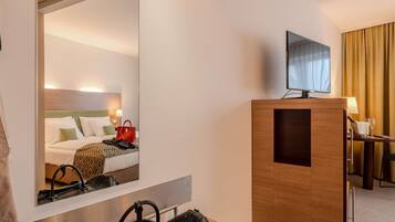 A hotel room with a large mirror reflecting the bed and a television on a wooden stand.