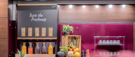 A juice bar with a sign reading 'Juice Bar' and 'Taste the Freshness.' There are various juice bottles and a wooden crate with fruits.